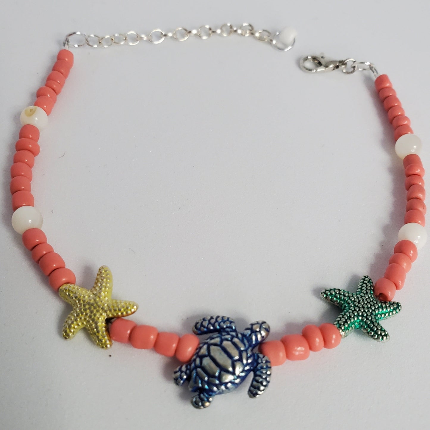 Anklet with coral beads, starfish, and turtle charm on a white background