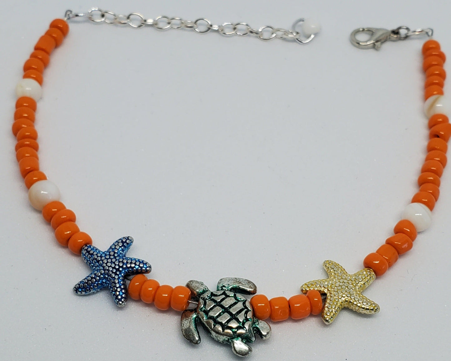 Anklet with orange beads, starfish, and turtle charms on a white background