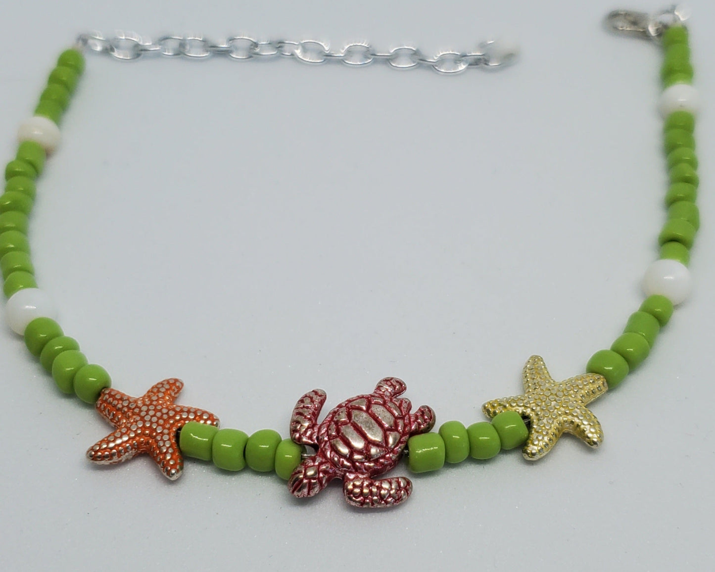 Anklet with green beads, starfish, and turtle charms on a light gray background