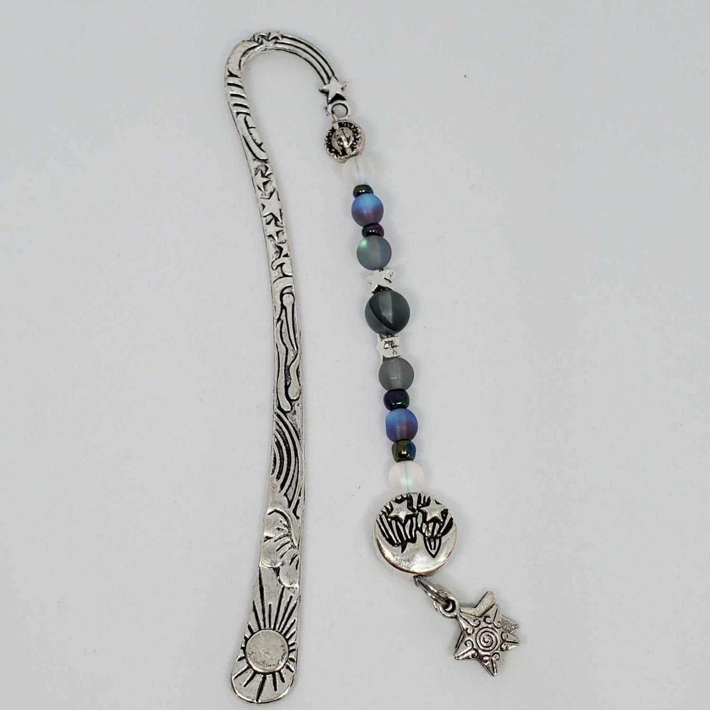 Metal celestial bookmark with engraved sun design, adorned with gray and purple aura glass beads, pewter star charms, and dangling star pendant