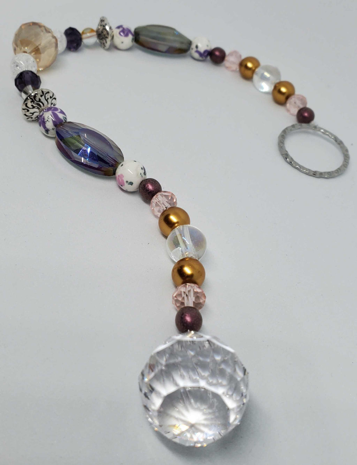 Purple and gold floral crystal suncatcher with teardrop prism and porcelain beads hanging in sunlight