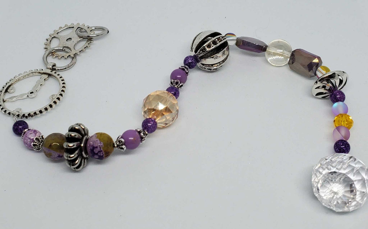 Steampunk purple crystal suncatcher with gold and purple beads and industrial pewter accents hanging on a plain background