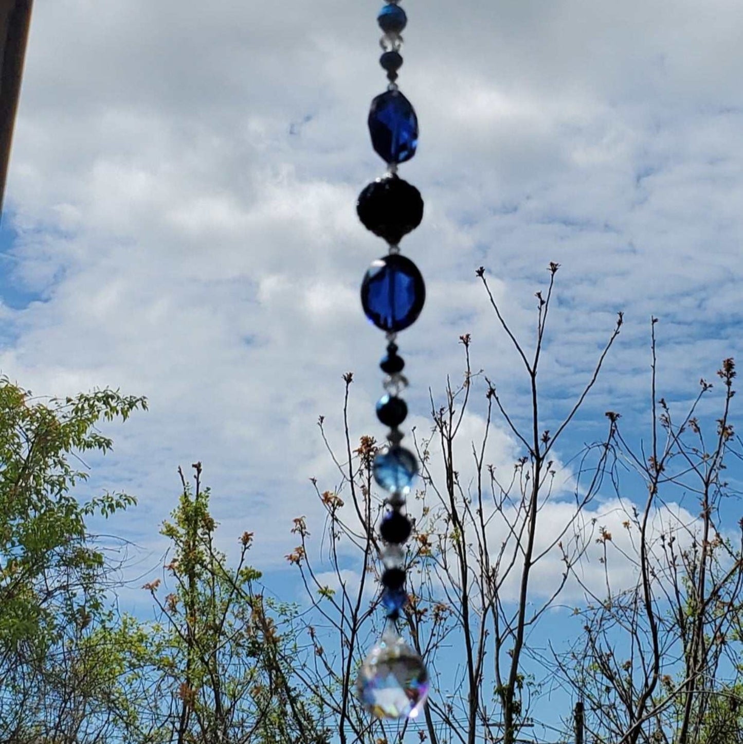 Navy and cobalt blue crystal suncatcher with teardrop prism hanging outdoors against a cloudy sky background