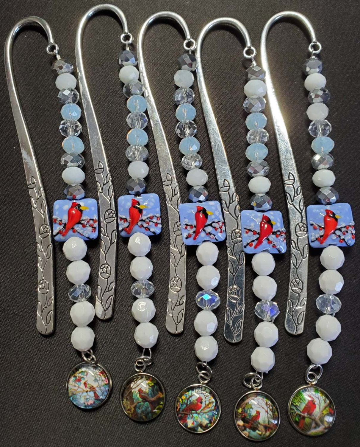 Set of six metal cardinal bookmarks with winter-themed beads and colorful cardinal charms on black background