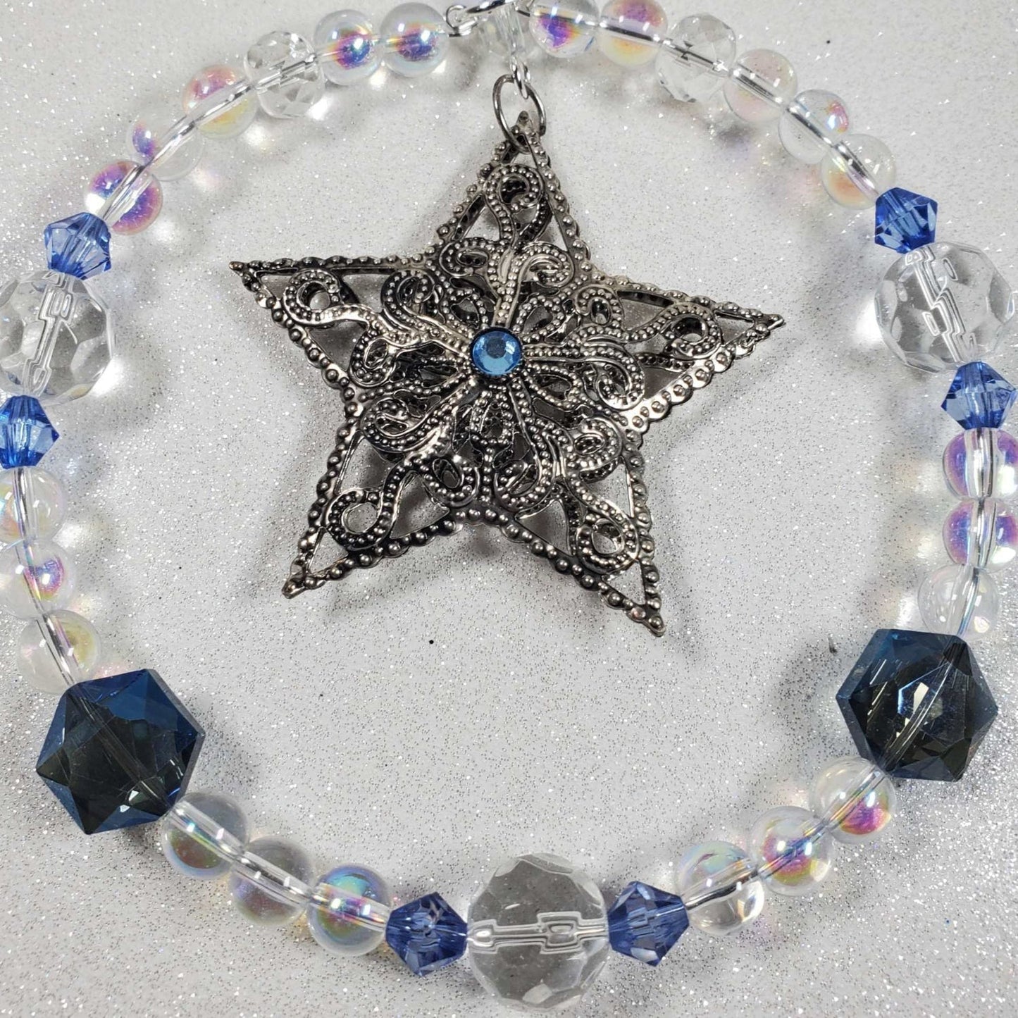Holiday ornament featuring a pewter filigree star with blue glass bead accents and clear beads in a circular design.
