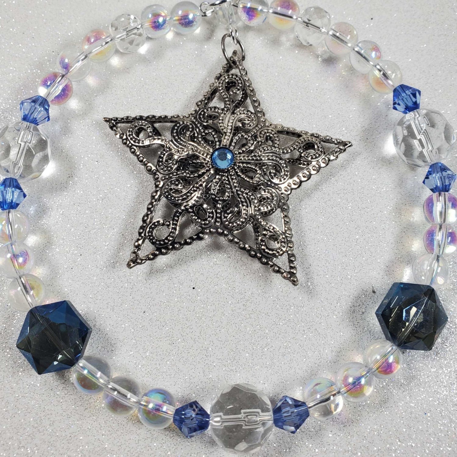 Holiday ornament featuring a pewter filigree star with blue glass bead accents and clear beads in a circular design.