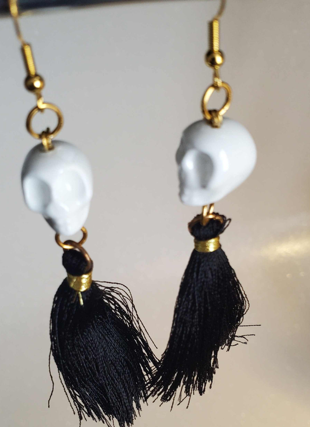 Día De Los Muertos skull earrings with white ceramic skulls and black tassels, gold hooks, festive and colorful jewelry accessory