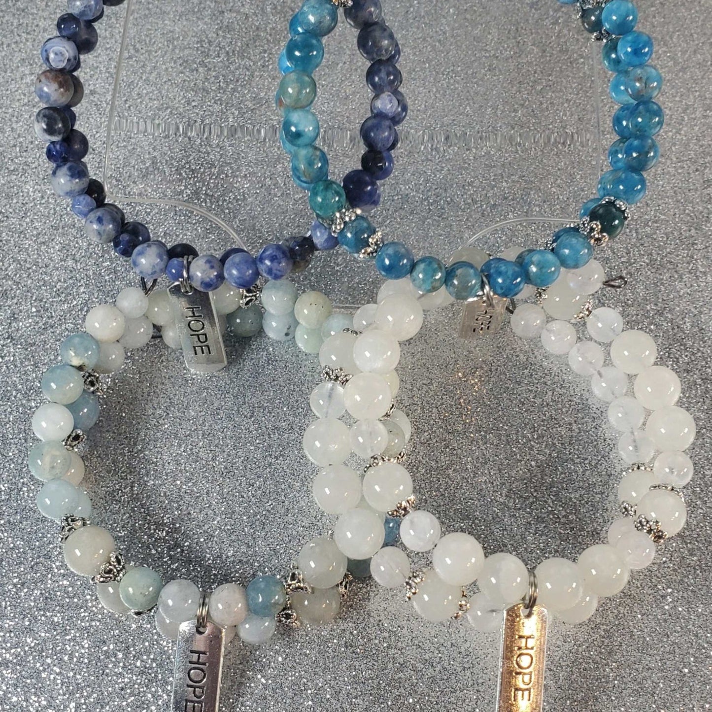 Set of four adjustable gemstone bracelets with pewter "Hope" charms, featuring blue, aqua, and white beads for inspiration and resilience.