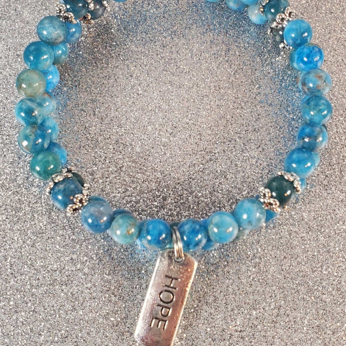 Blue gemstone bracelet with round beads and a pewter charm engraved with "Hope" on an adjustable memory wire cuff