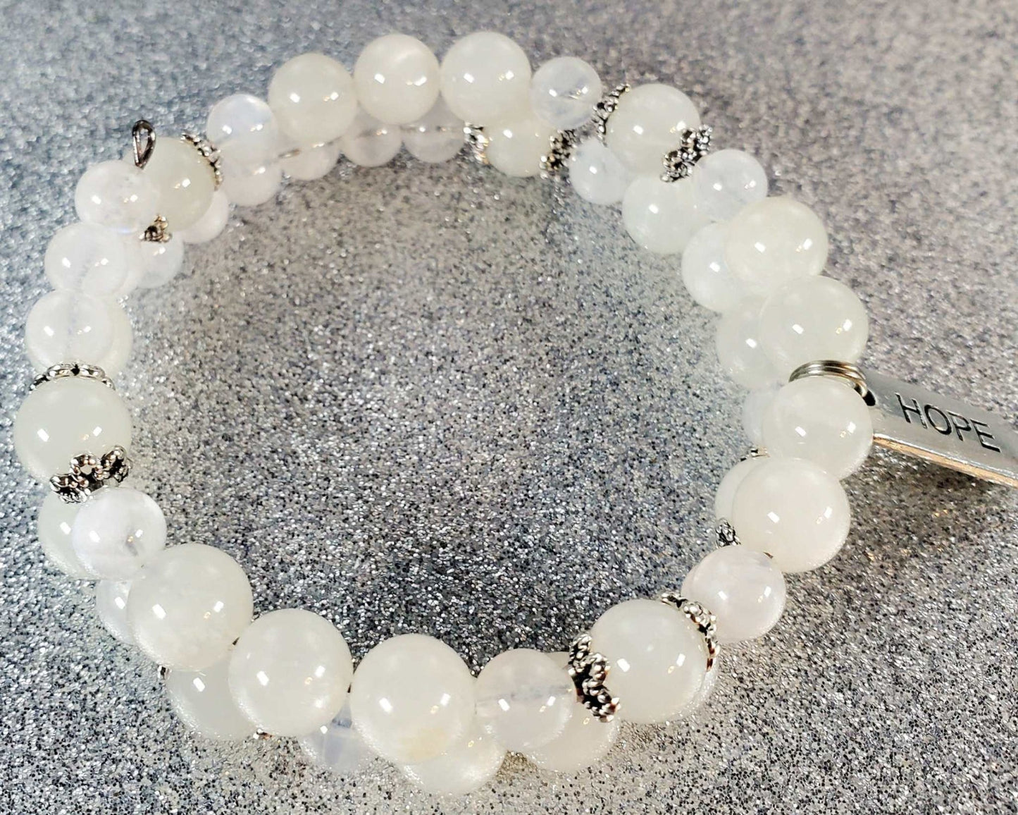 White gemstone bracelet with silver accents and a pewter charm engraved with the word "Hope" on a memory wire cuff.