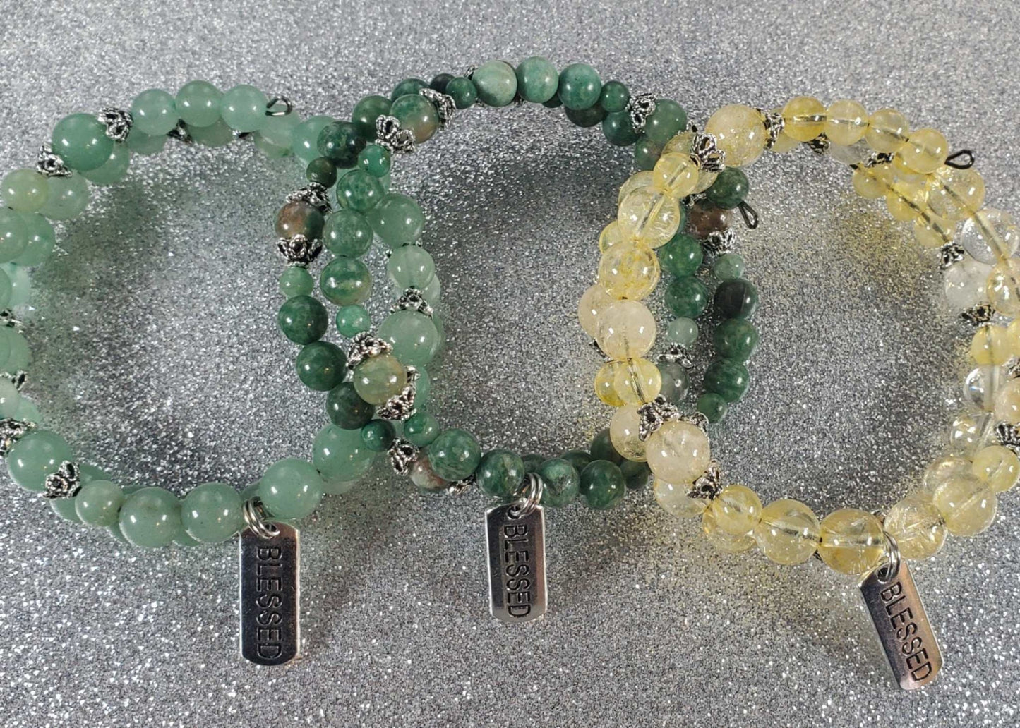 Three radiant gemstone bracelets with green and yellow beads, each featuring a pewter charm engraved with "Blessed" on memory wire.