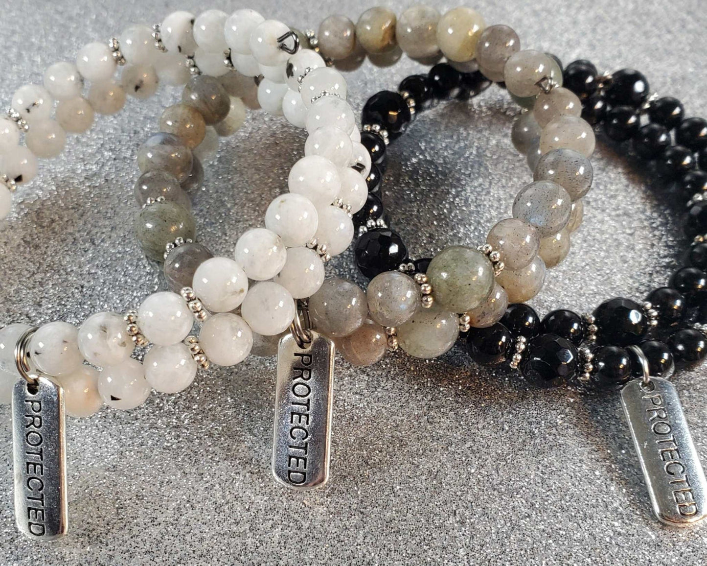 Handcrafted gemstone bracelet with "Protected" pewter charm featuring white, gray, and black beads on flexible memory wire for adjustable fit.