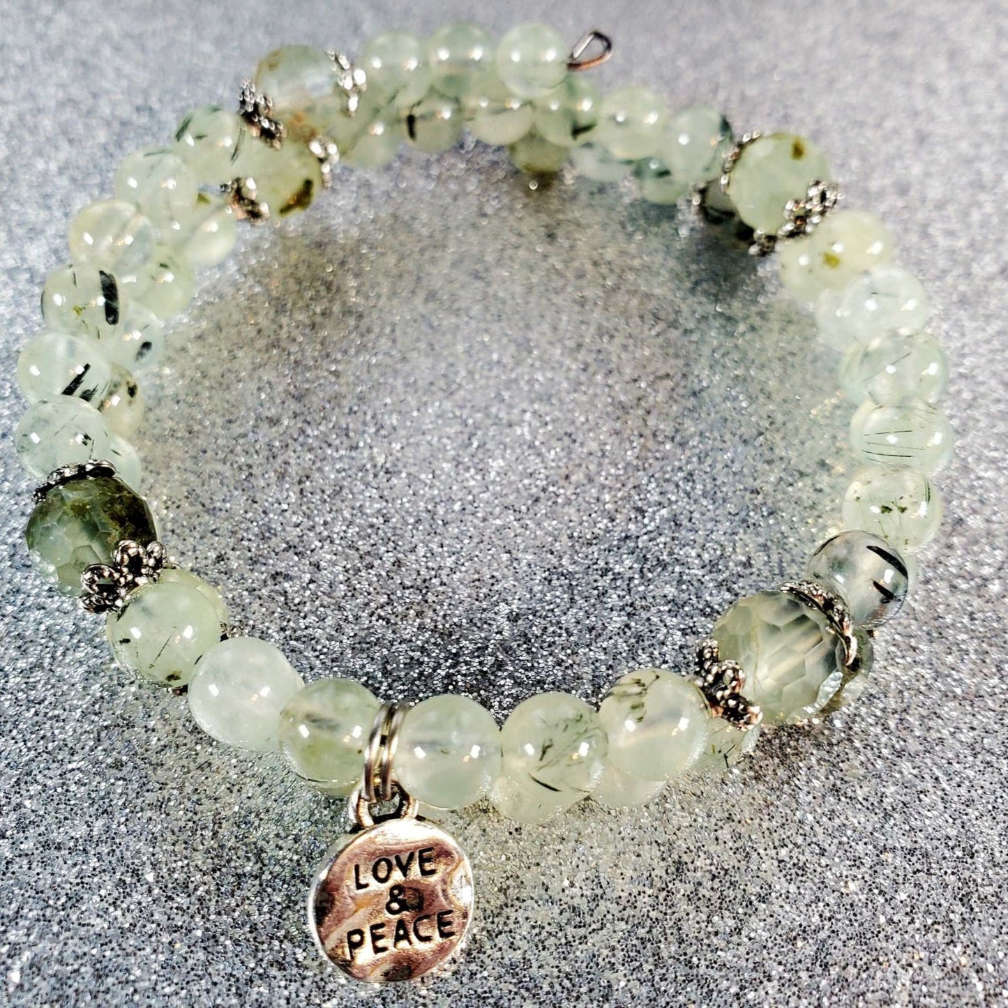 Gemstone bracelet with light green beads and a pewter charm inscribed with Love & Peace on memory wire band