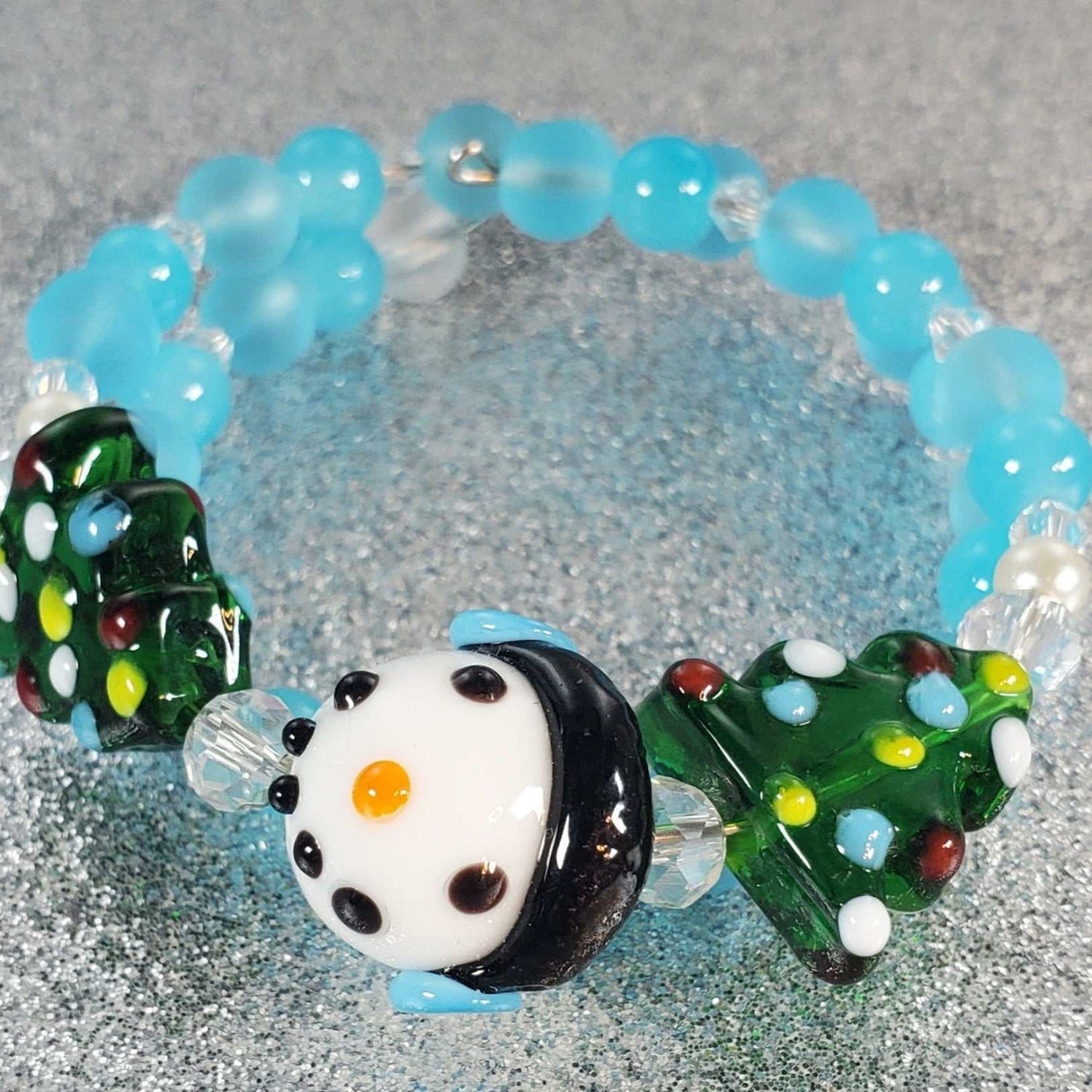 Child's holiday bracelet with festive snowman and decorated Christmas tree lampwork beads on blue and clear memory wire beads