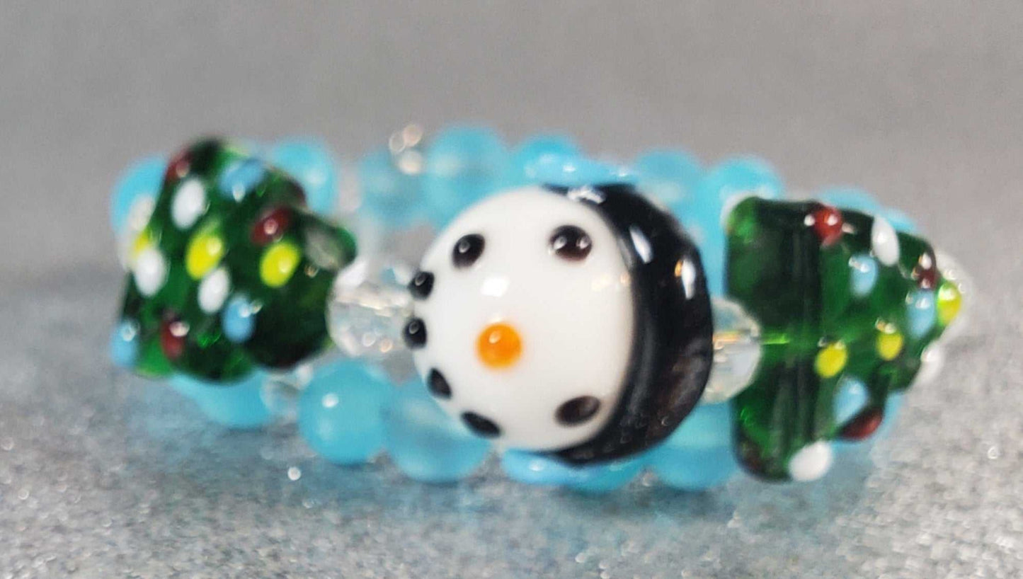 Child's holiday bracelet with festive snowman and Christmas tree lampwork beads on blue memory wire band