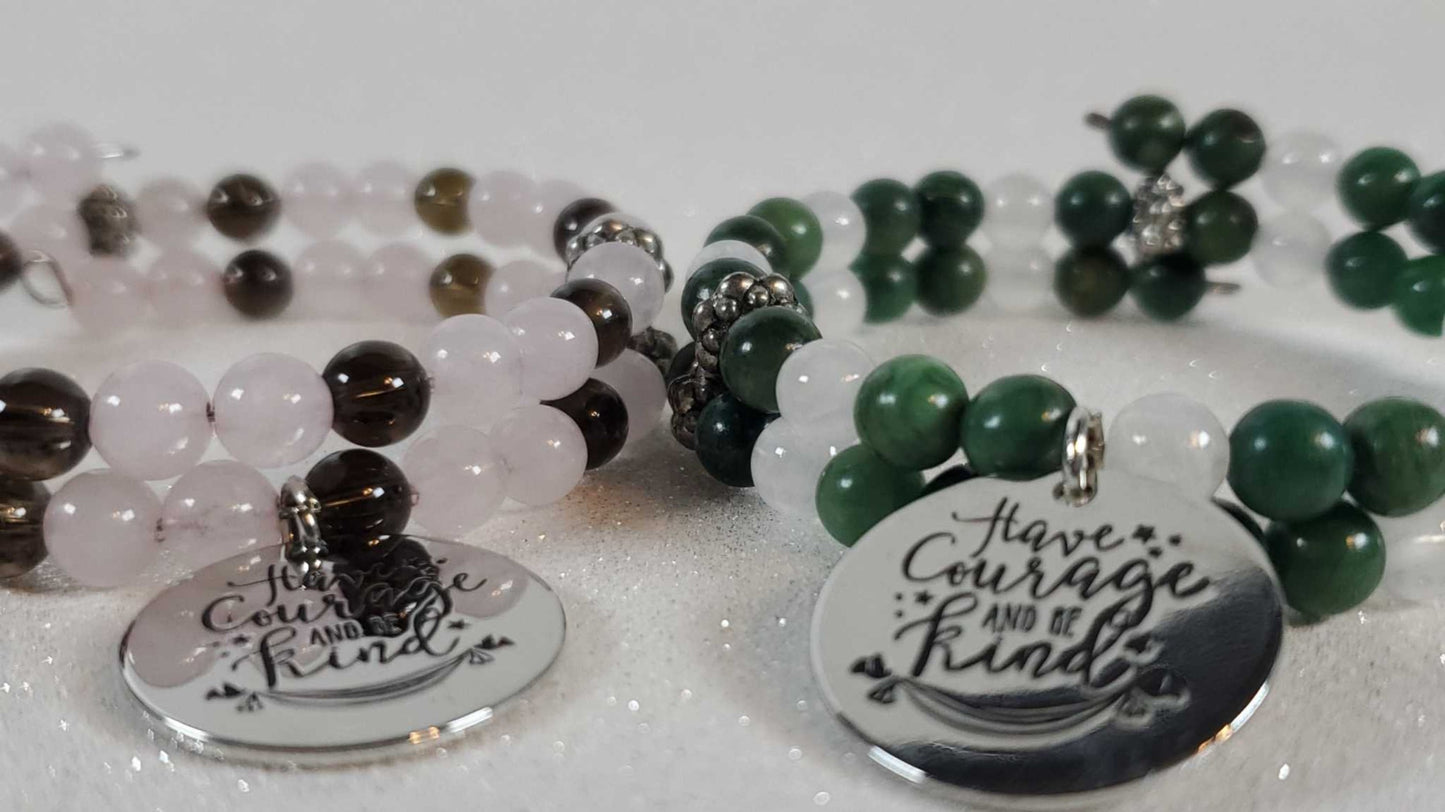 Close-up of gemstone bracelets with engraved "Have Courage Be Kind" charms featuring rose quartz, smoky quartz, green jade, and selenite beads