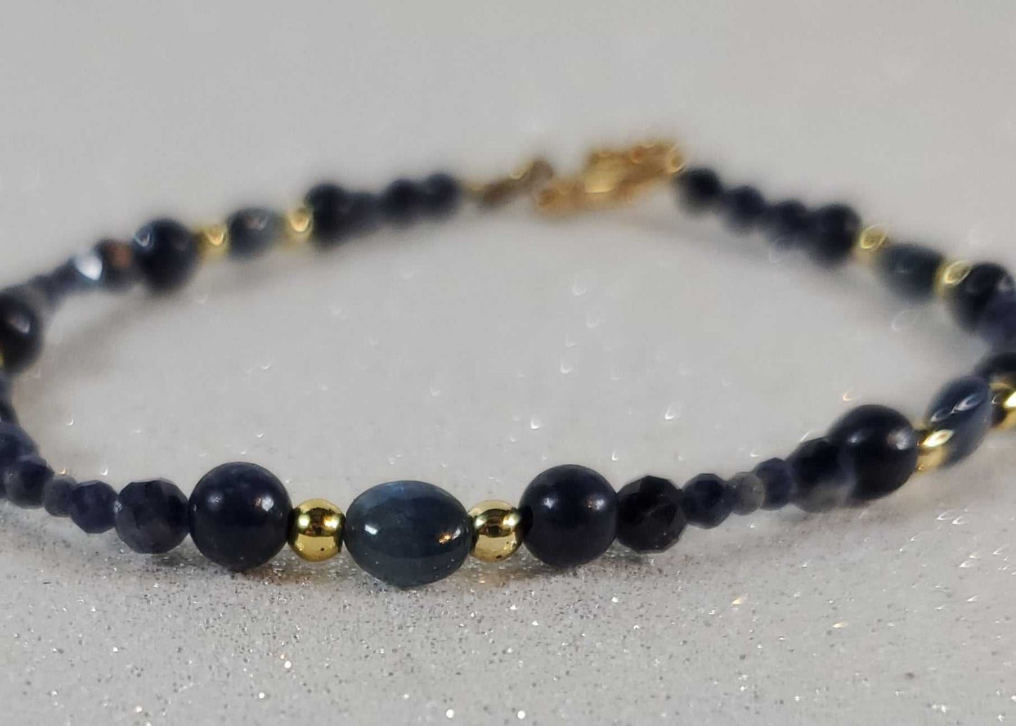 Sapphire and Tanzanite gemstone bracelet with brass accents and lobster clasp on sparkling surface
