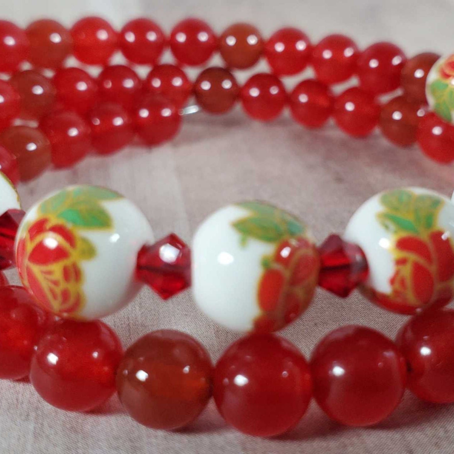 Red gemstone and porcelain floral bead bracelet with hand-painted flowers on white beads and red round beads on memory wire.