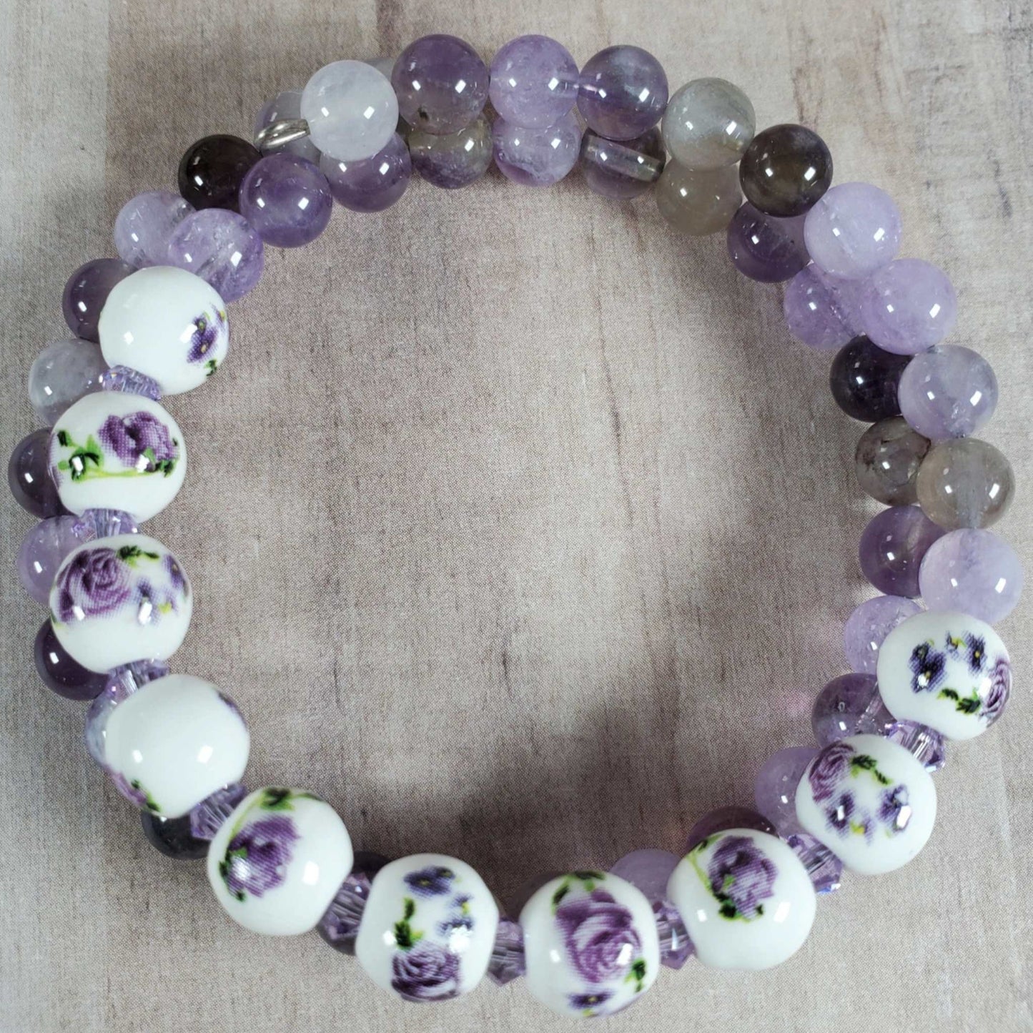 Floral bracelet with amethyst gemstones and porcelain beads featuring purple rose designs on memory wire.