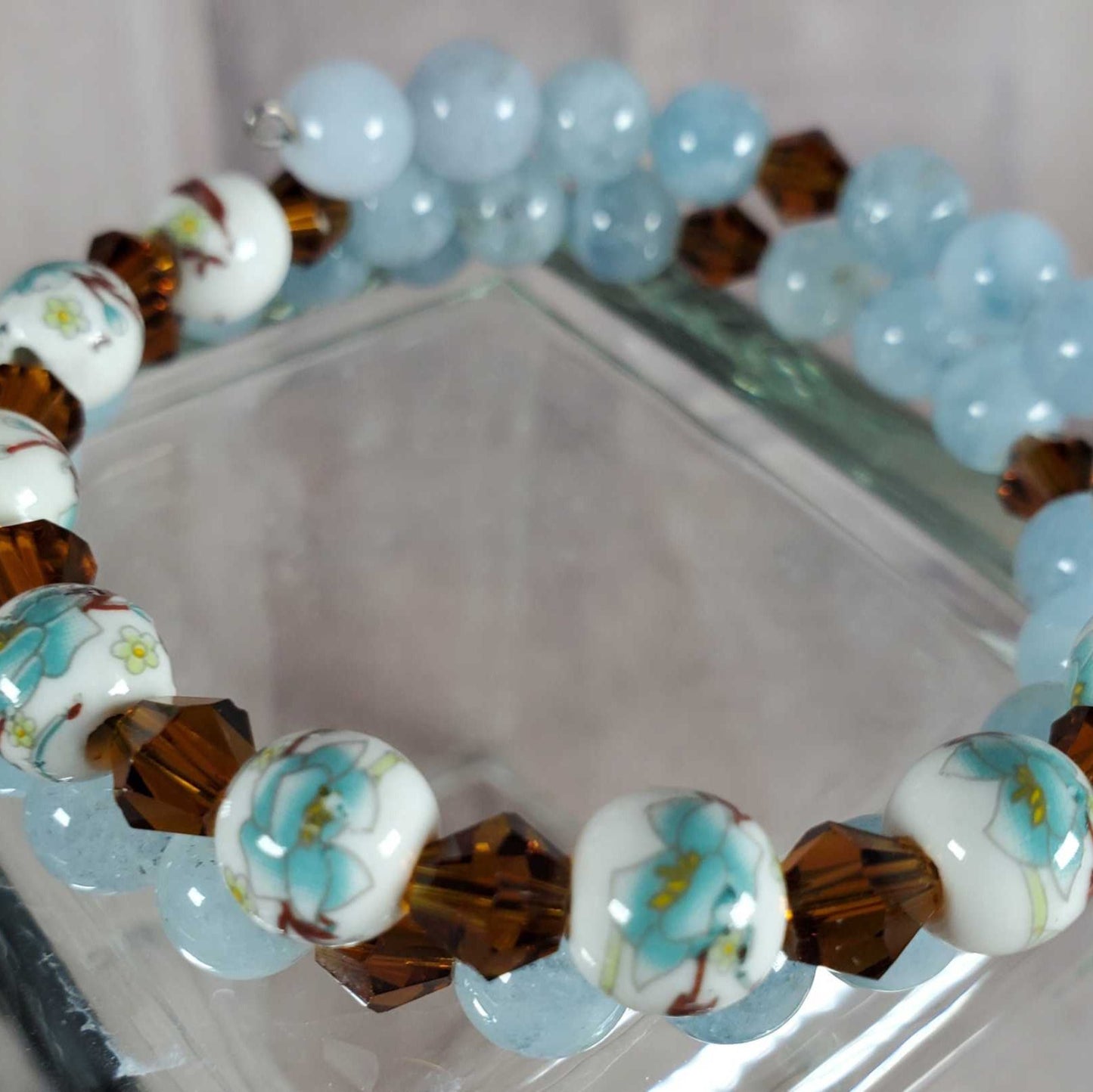 Floral bracelet with porcelain floral beads, blue gemstones, and brown faceted accents on memory wire.