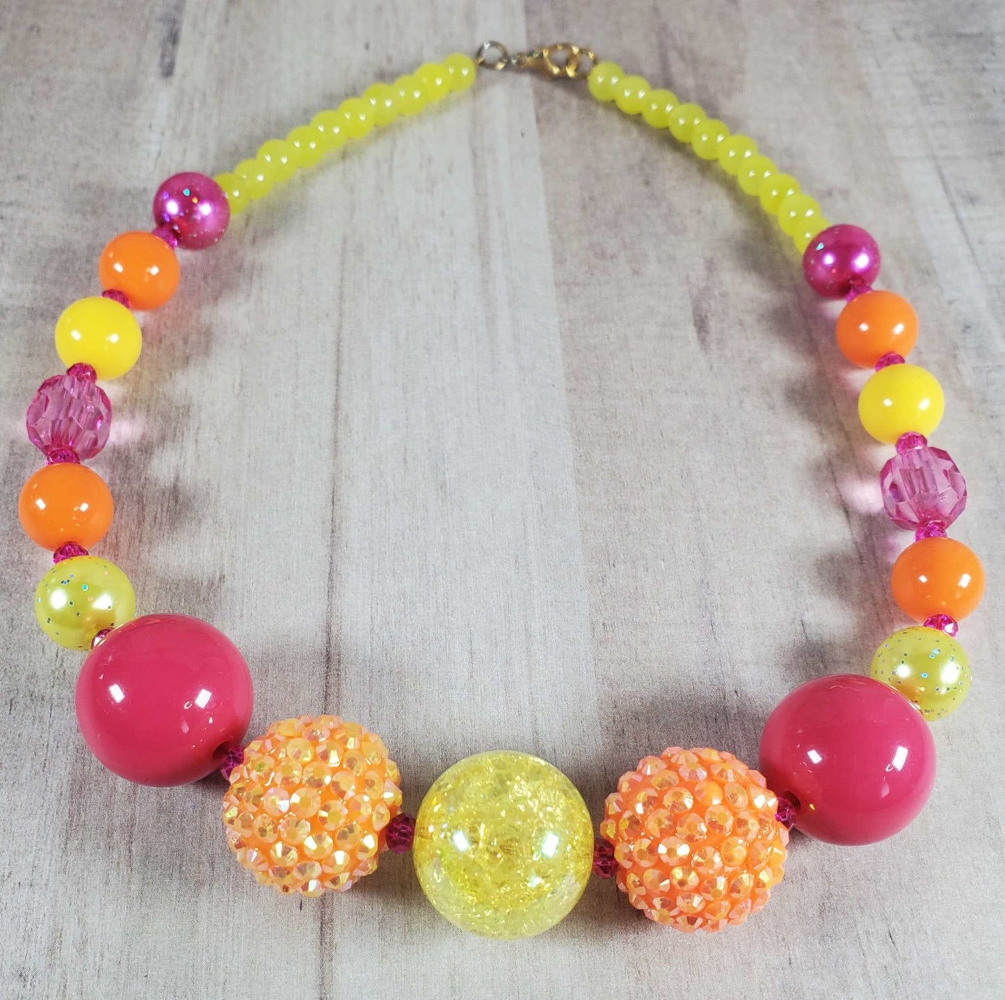 Colorful neon beaded necklace with yellow, orange, and pink beads on wooden background