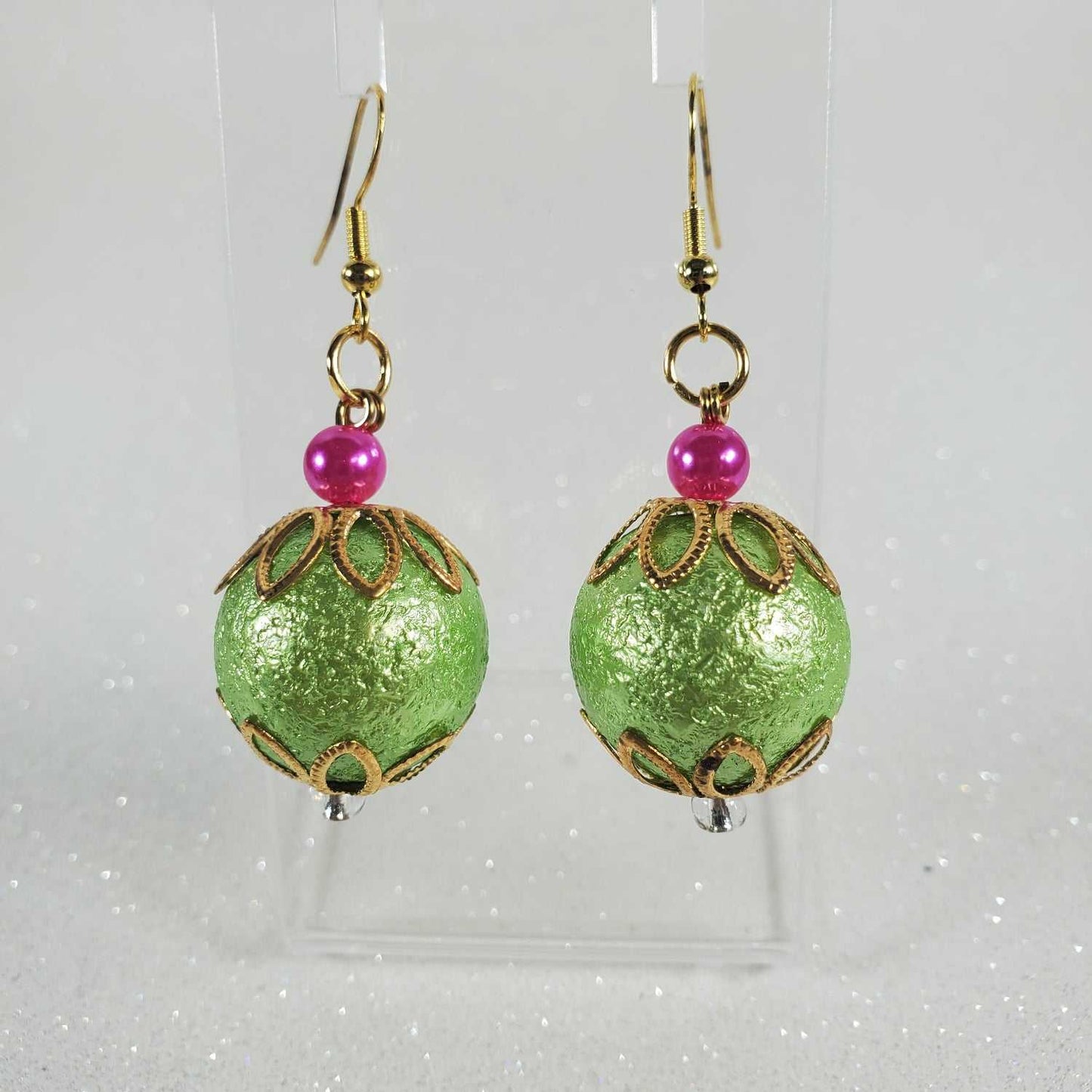 Green beaded earrings with pink beads on a clear card against a white background