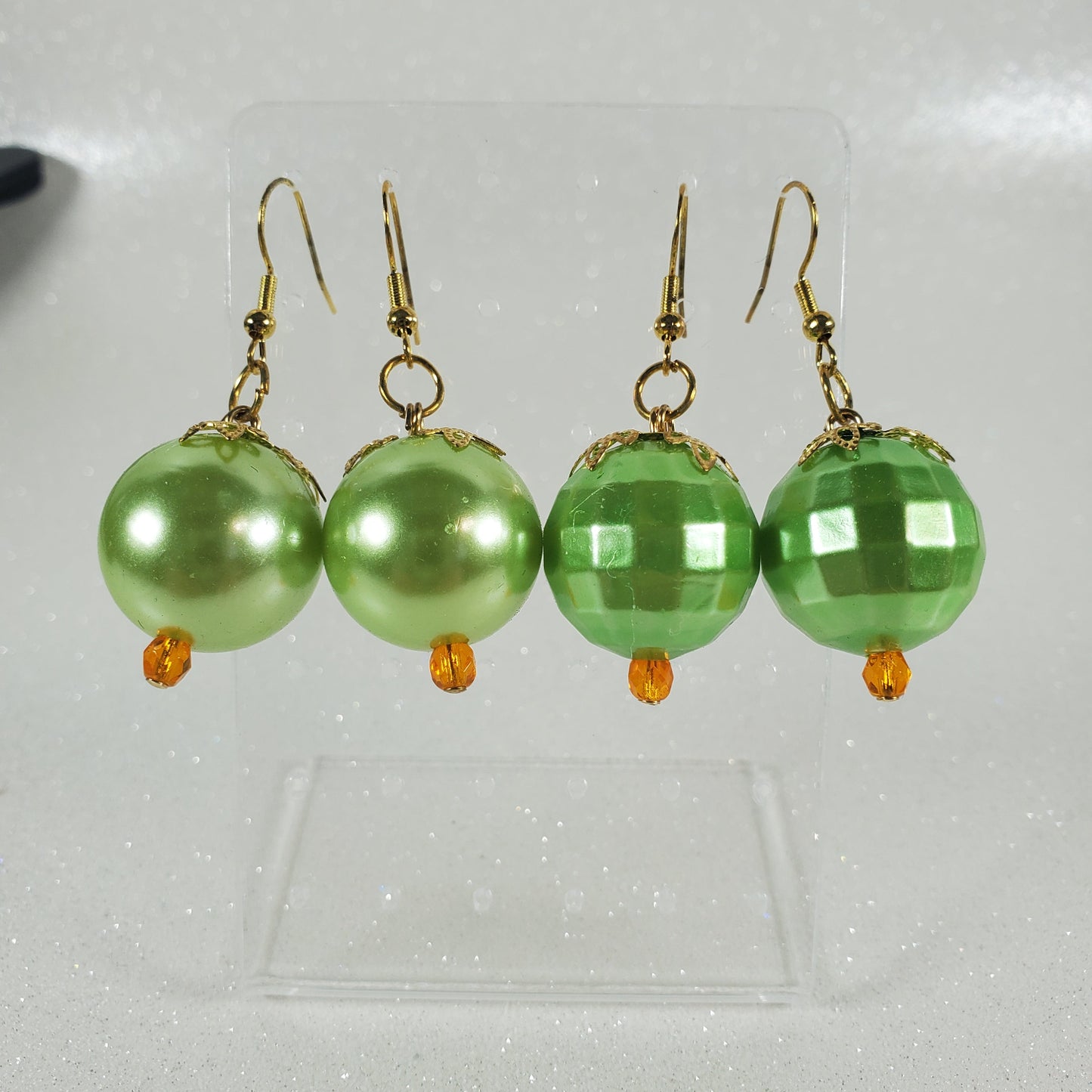 Green beaded earrings on a reflective surface