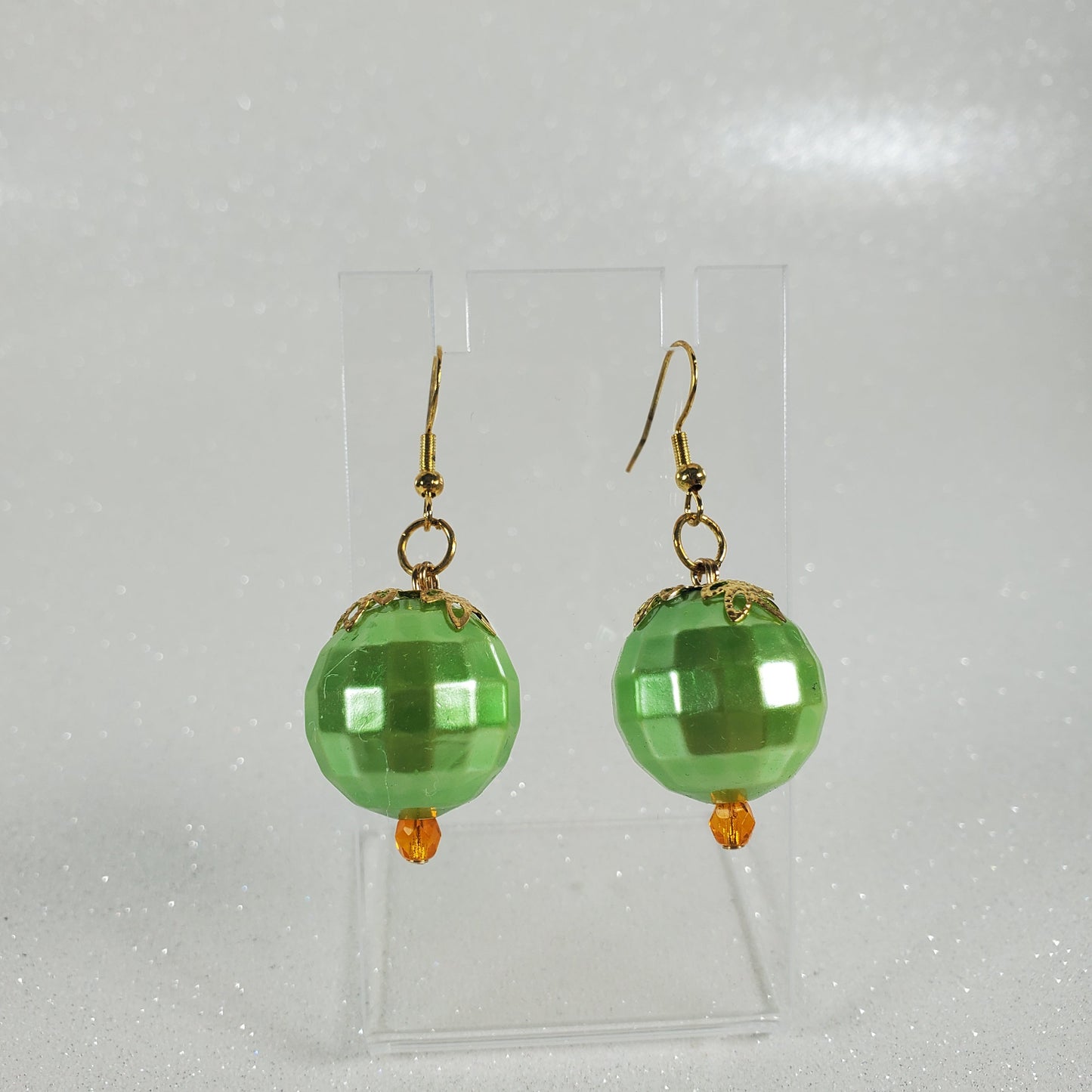 Green beaded earrings on a clear plastic stand against a light gray background