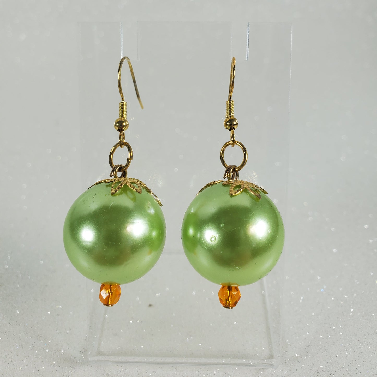 Green pearl earrings with gold hooks on a clear background