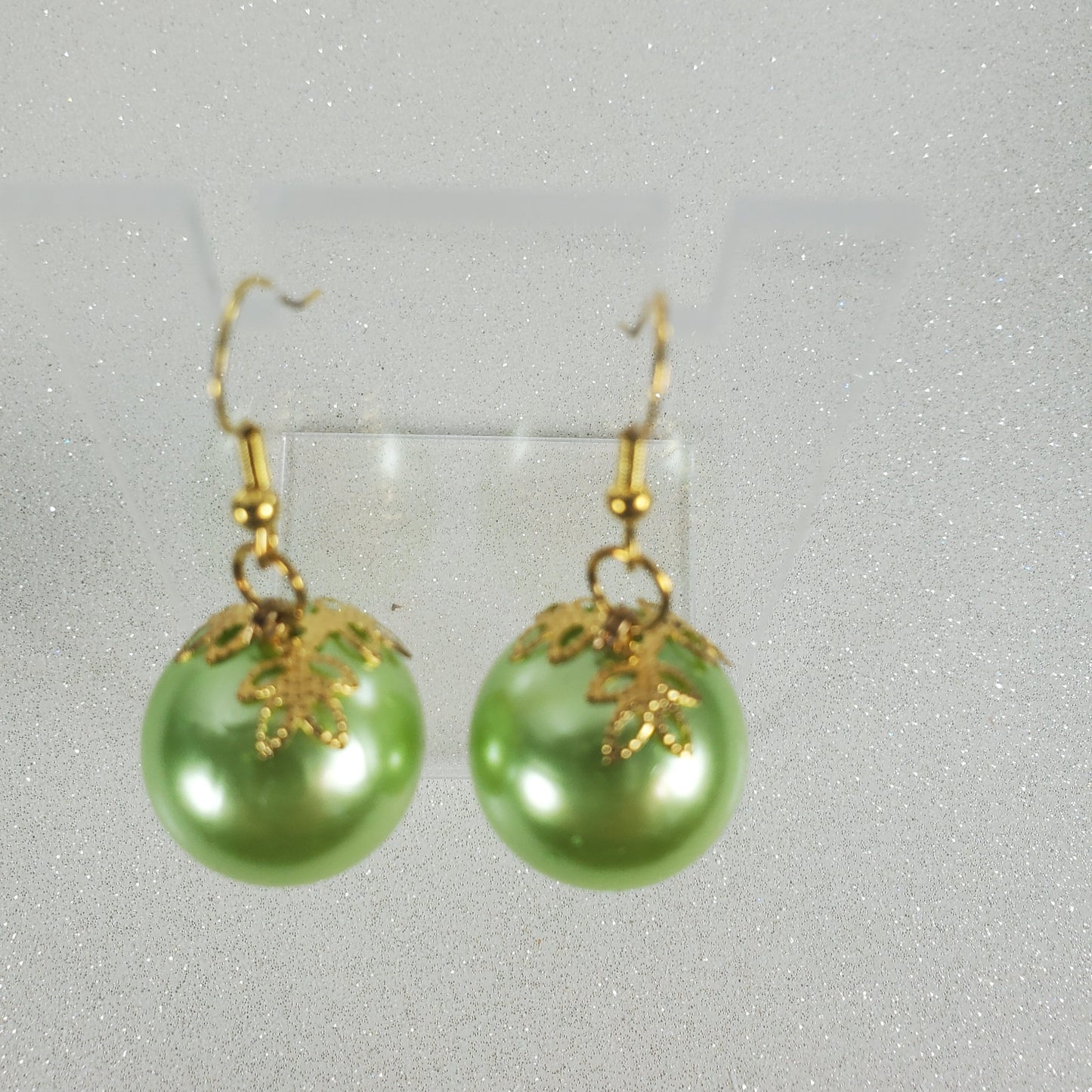 Green pearl earrings with gold accents on a gray background