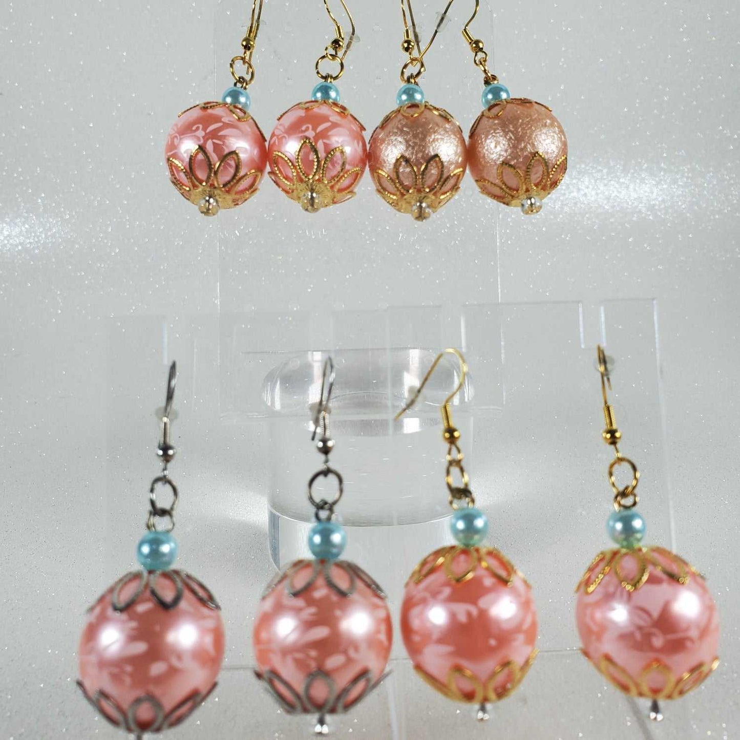 Pair of pink beaded earrings on a clear stand against a light gray background