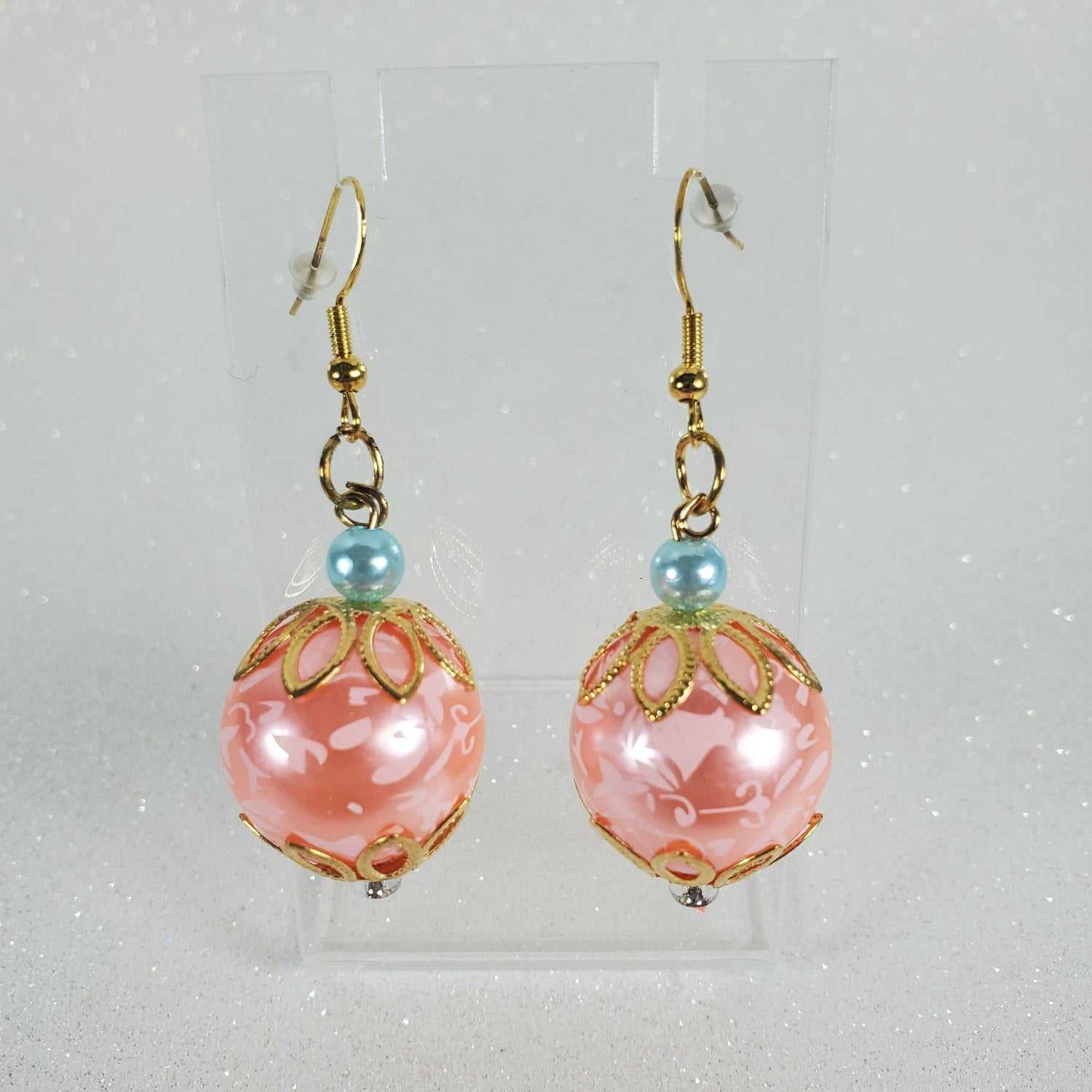 Pair of peach earrings with gold accents and blue beads on a light gray background