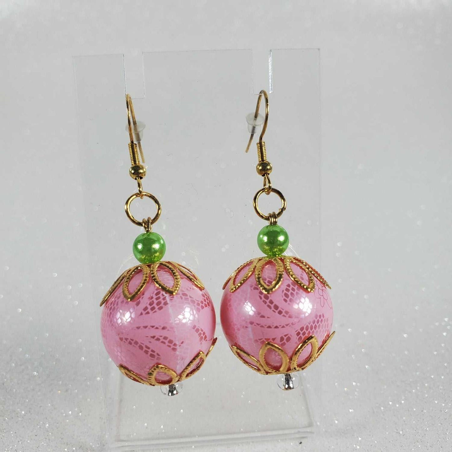 Pair of pink beaded earrings with gold accents and green beads on a white background