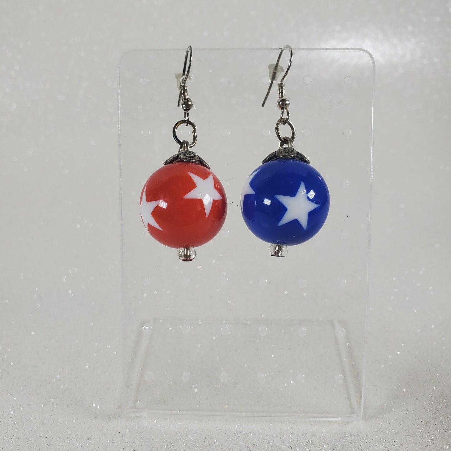 Pair of earrings with blue and red beads featuring white stars on a clear background