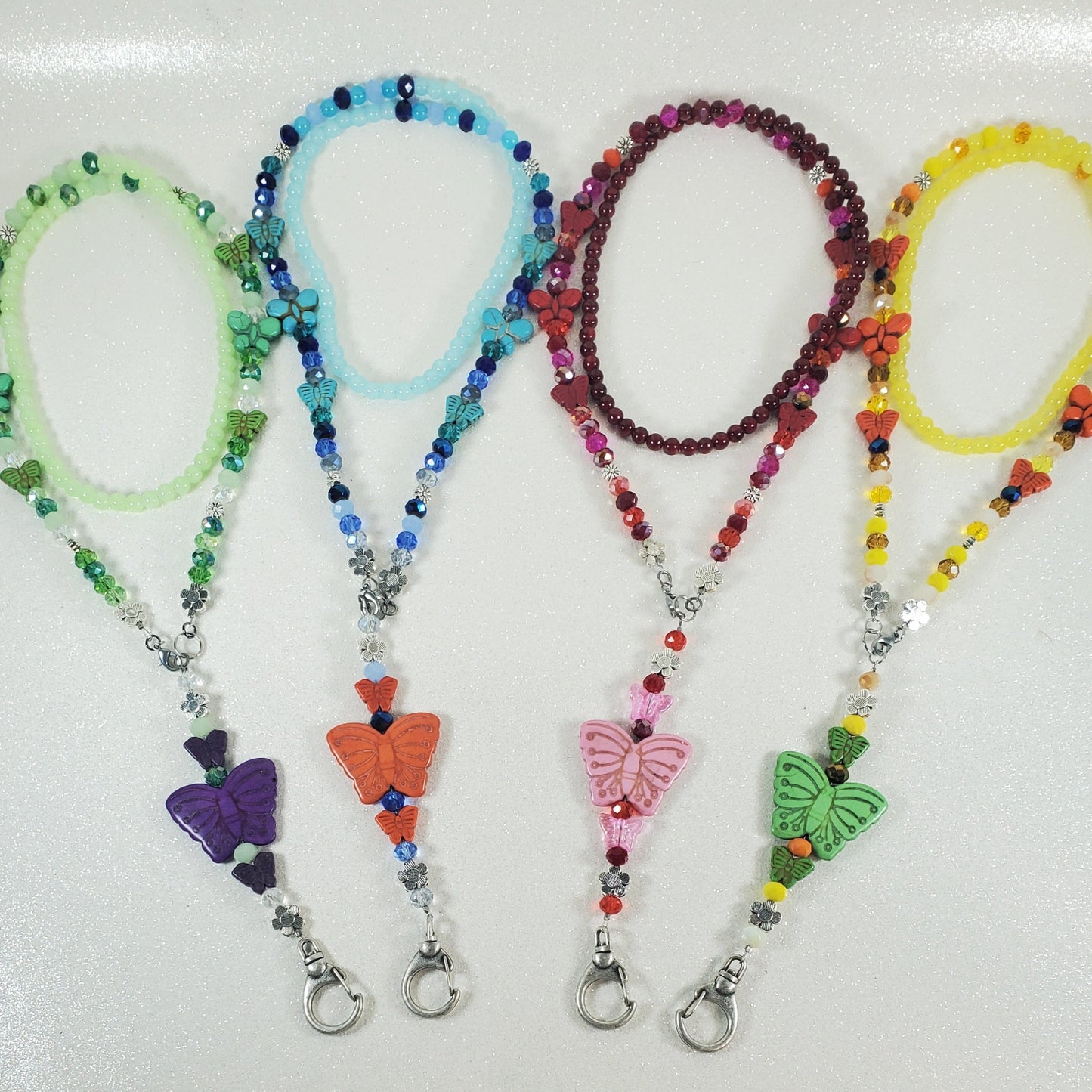 Four colorful beaded lanyards with butterfly charms on a white background