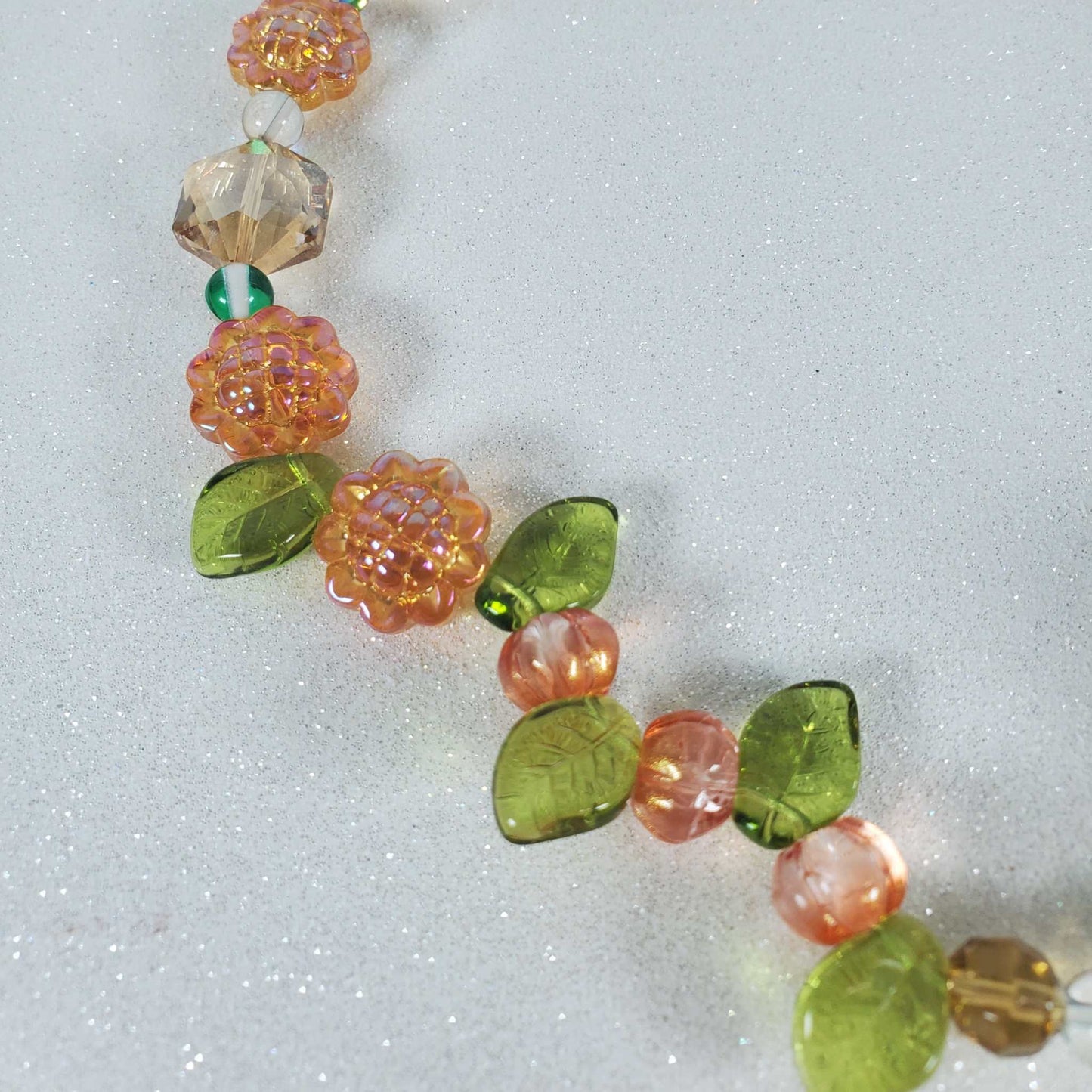 Crystal suncatcher with orange sunflower beads, green glass leaves, and yellow crystals on a glittery background