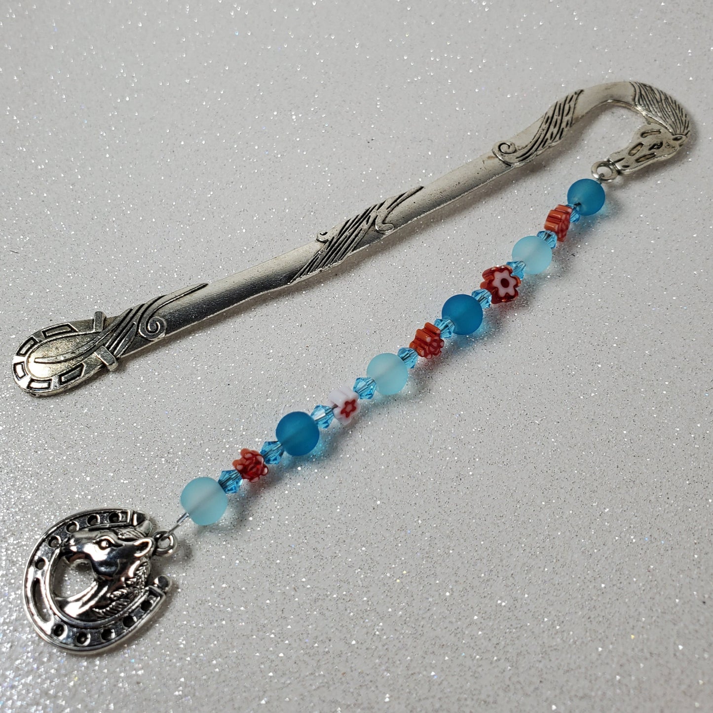 Silver bookmark with blue and red beads and a horse pendant on a gray background