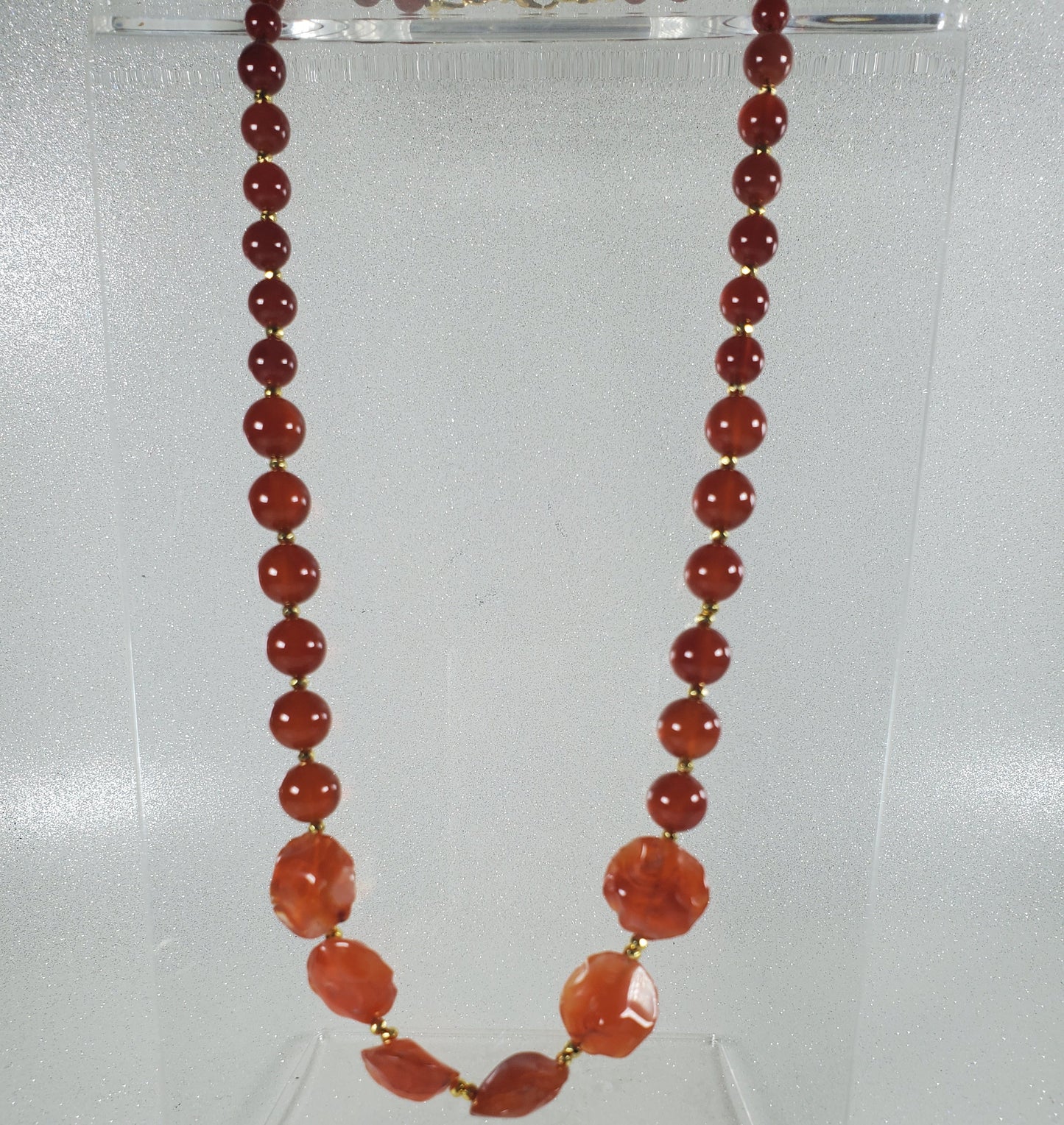 Necklace with red beads on a clear stand against a white background