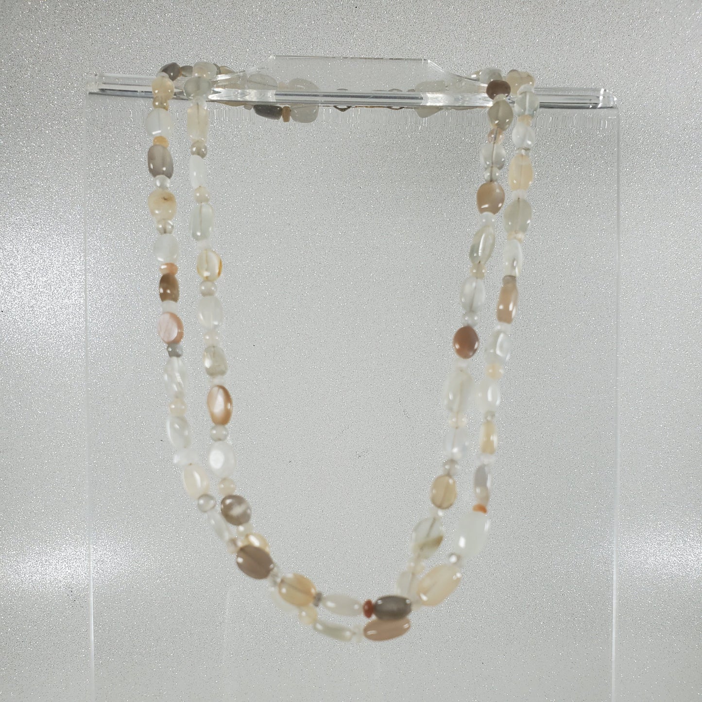 Necklace with multicolored beads on a clear stand against a light gray background