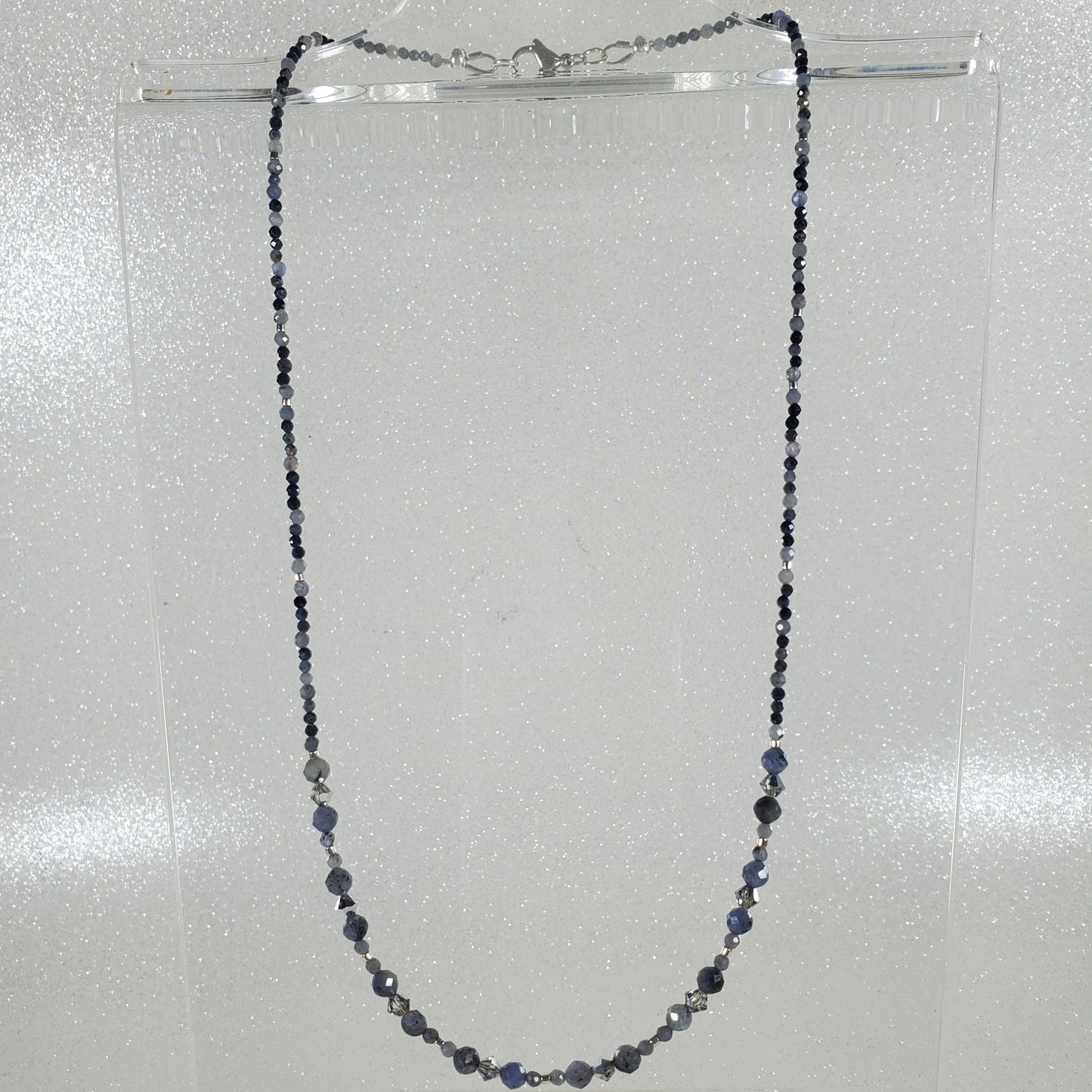 Necklace with small beads on a clear stand against a light gray background
