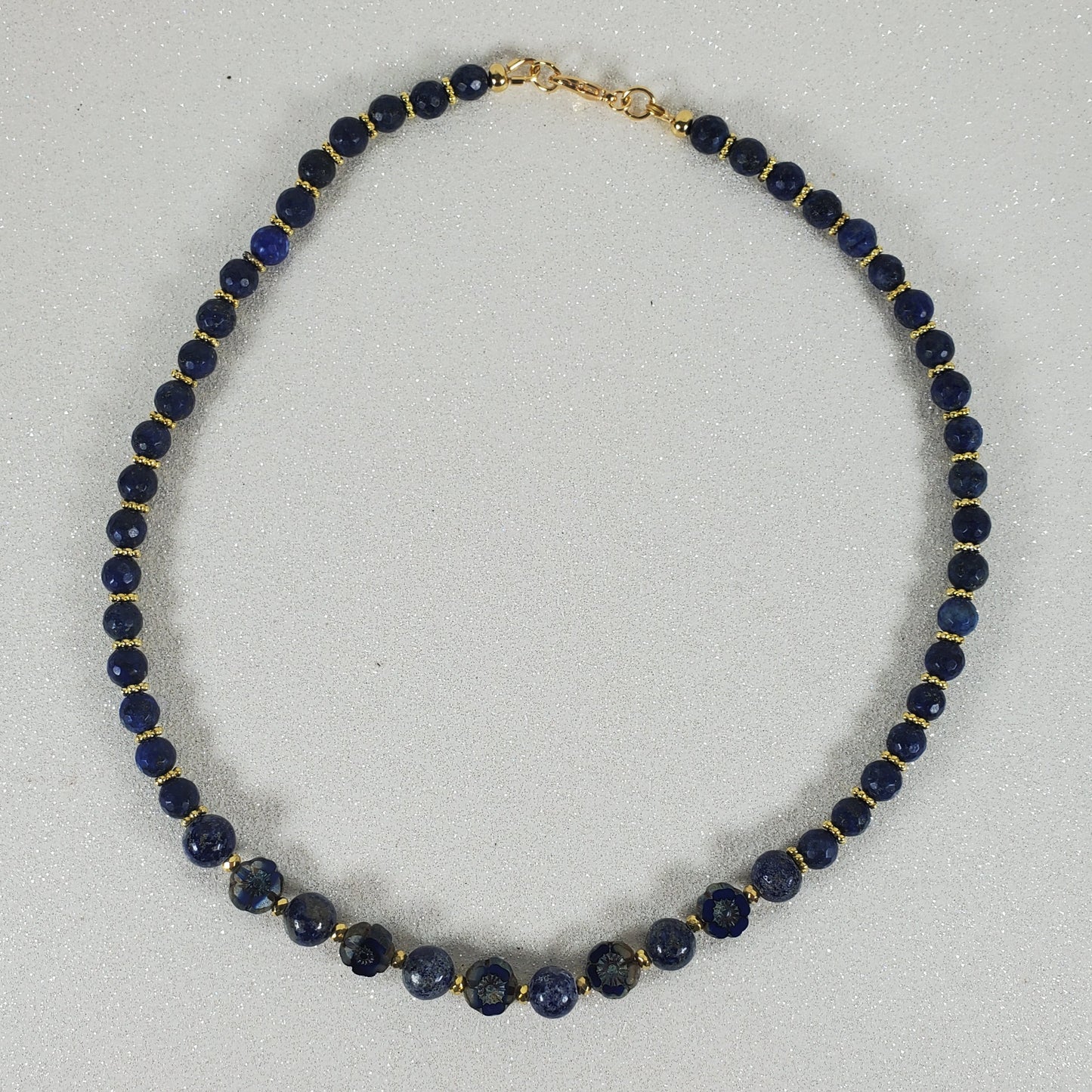 Necklace with blue beads and gold clasp on a light gray background