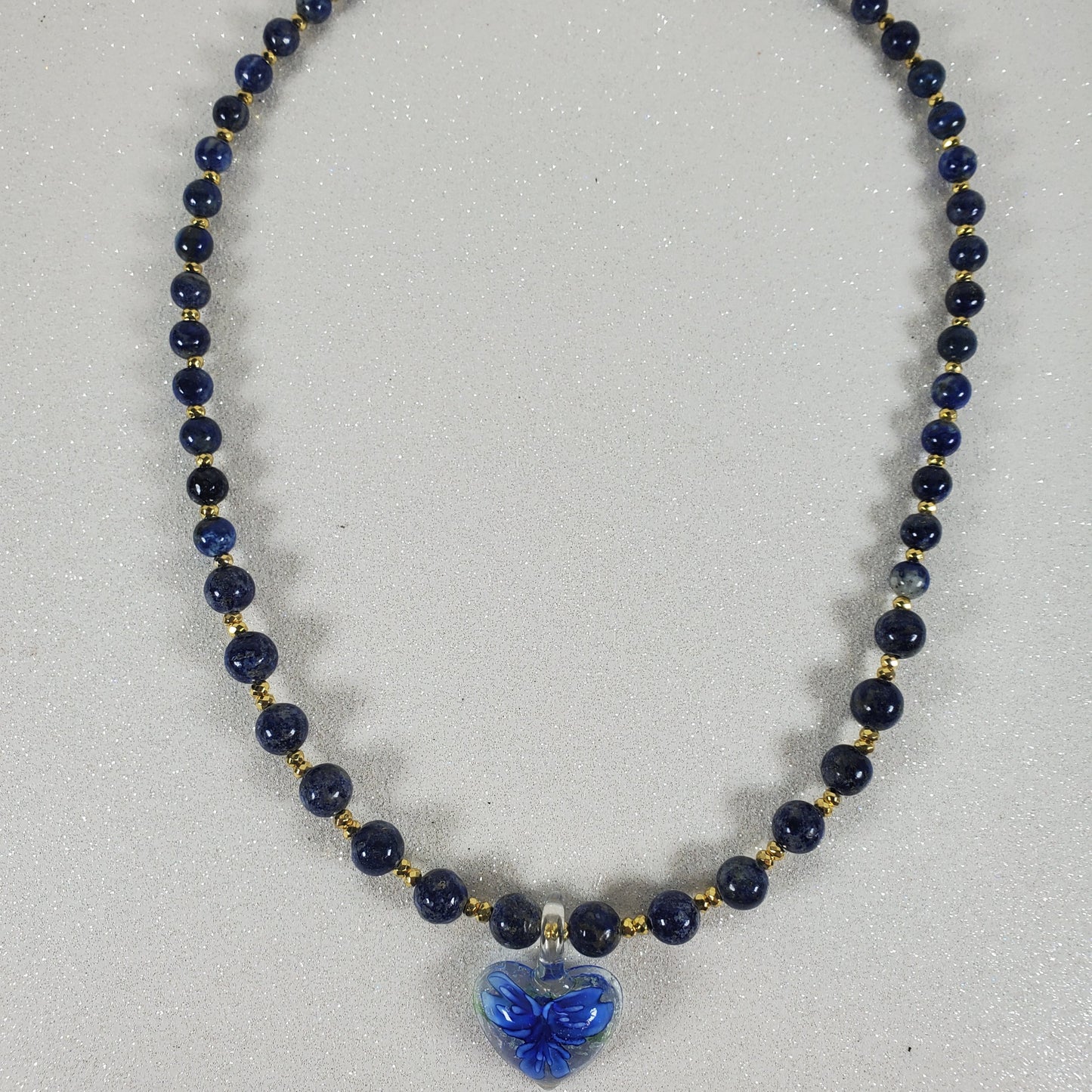 Necklace with blue beads and a blue flower pendant on a light gray background