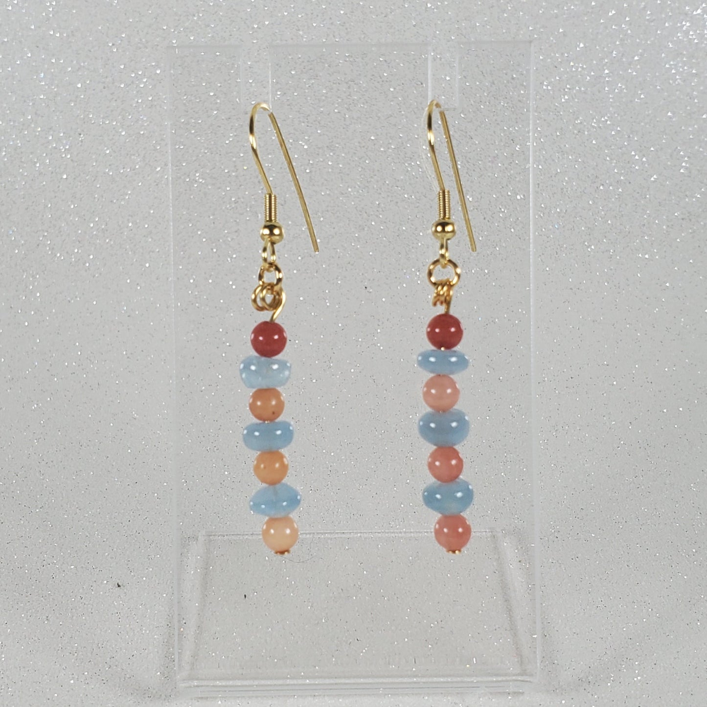 Pair of beaded earrings on a clear stand against a light gray background