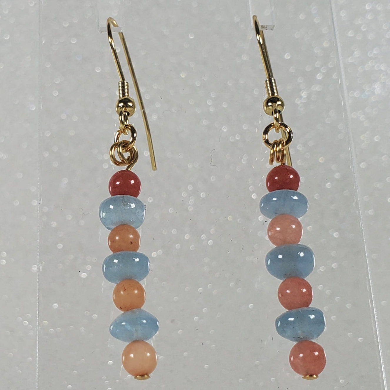 Pair of beaded earrings on a clear stand against a silver background