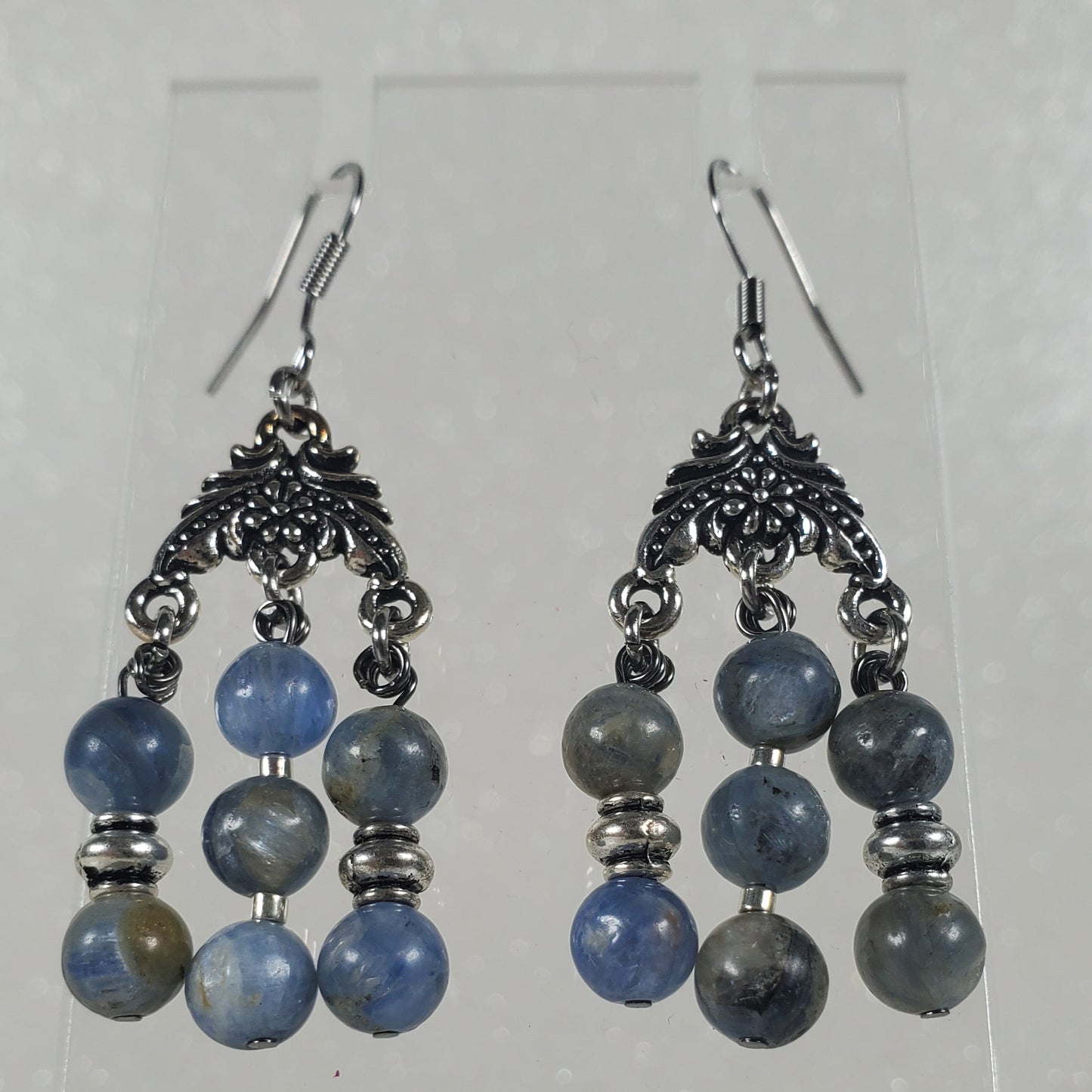 Pair of blue beaded earrings on a clear stand against a white background