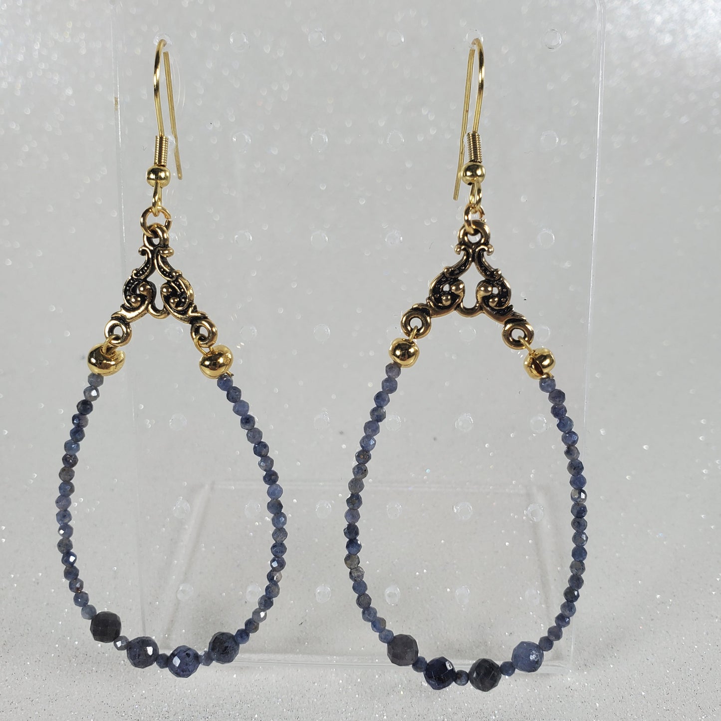 Beaded earrings with gold clasp on a clear card against a gray background