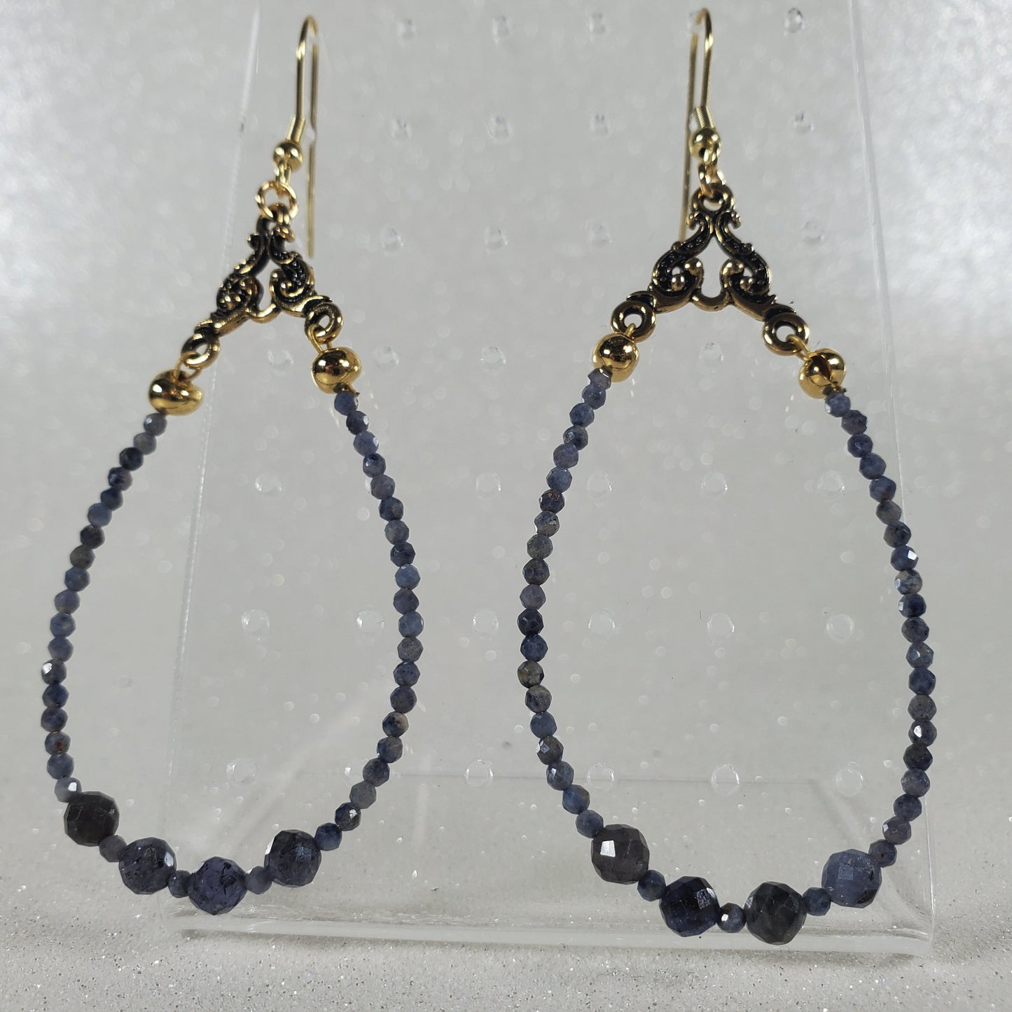 Pair of beaded earrings on a clear stand against a light gray background