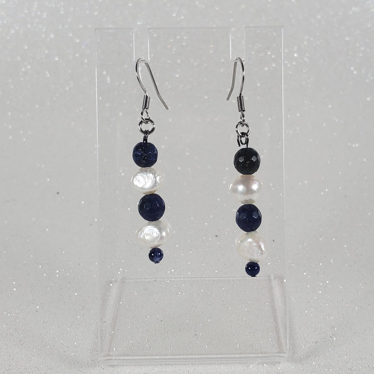 Pair of earrings on a clear plastic stand on a light gray background