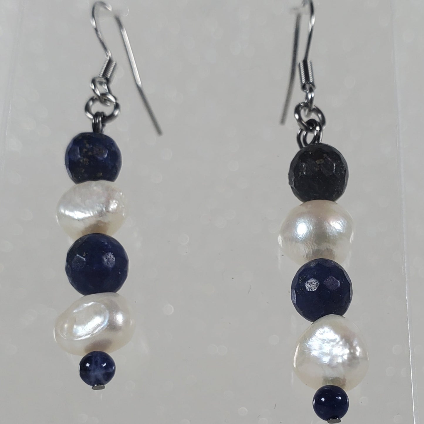Pair of earrings with blue and white beads on a clear stand against a light gray background