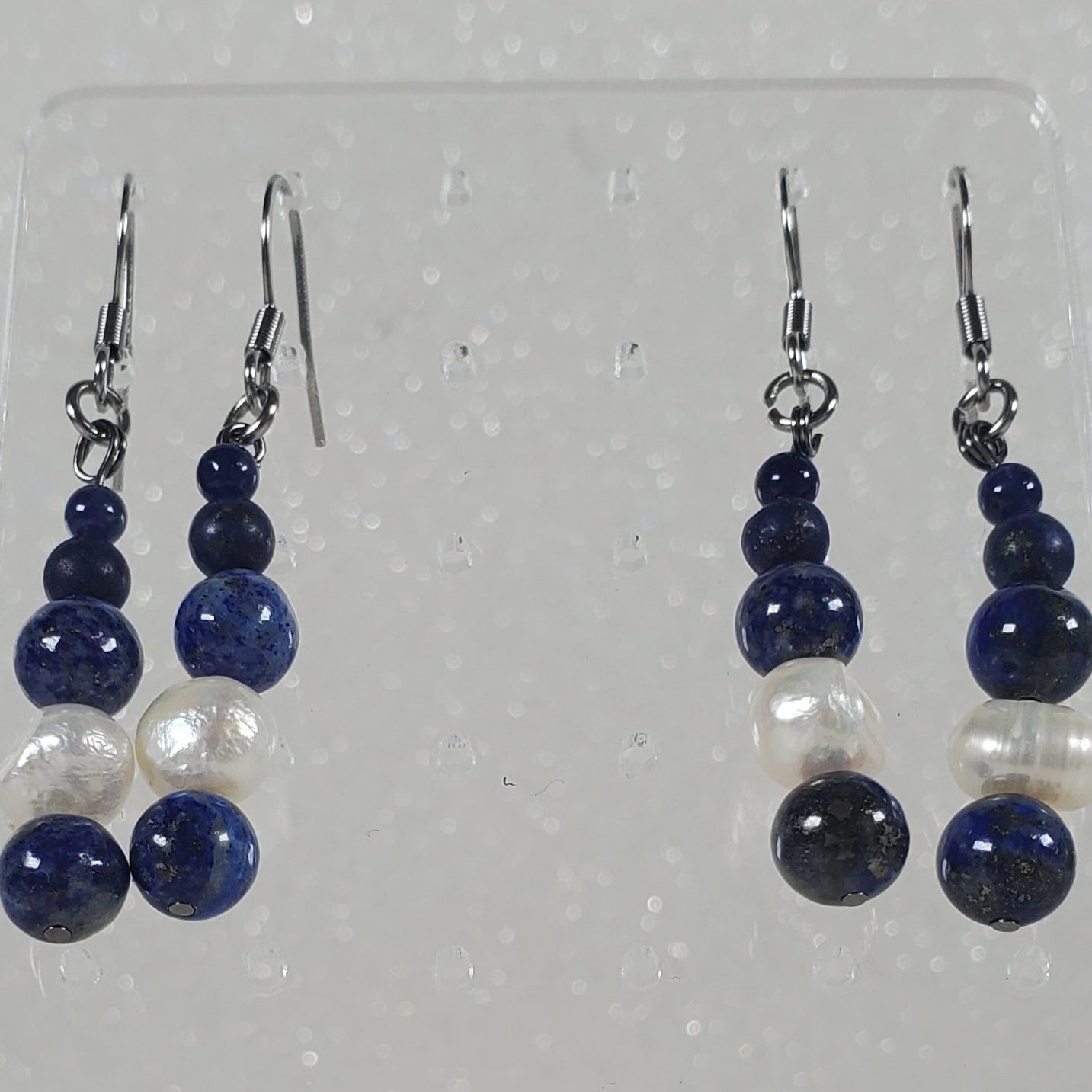 Pair of blue and white beaded earrings on a clear display card against a silver glittery background.